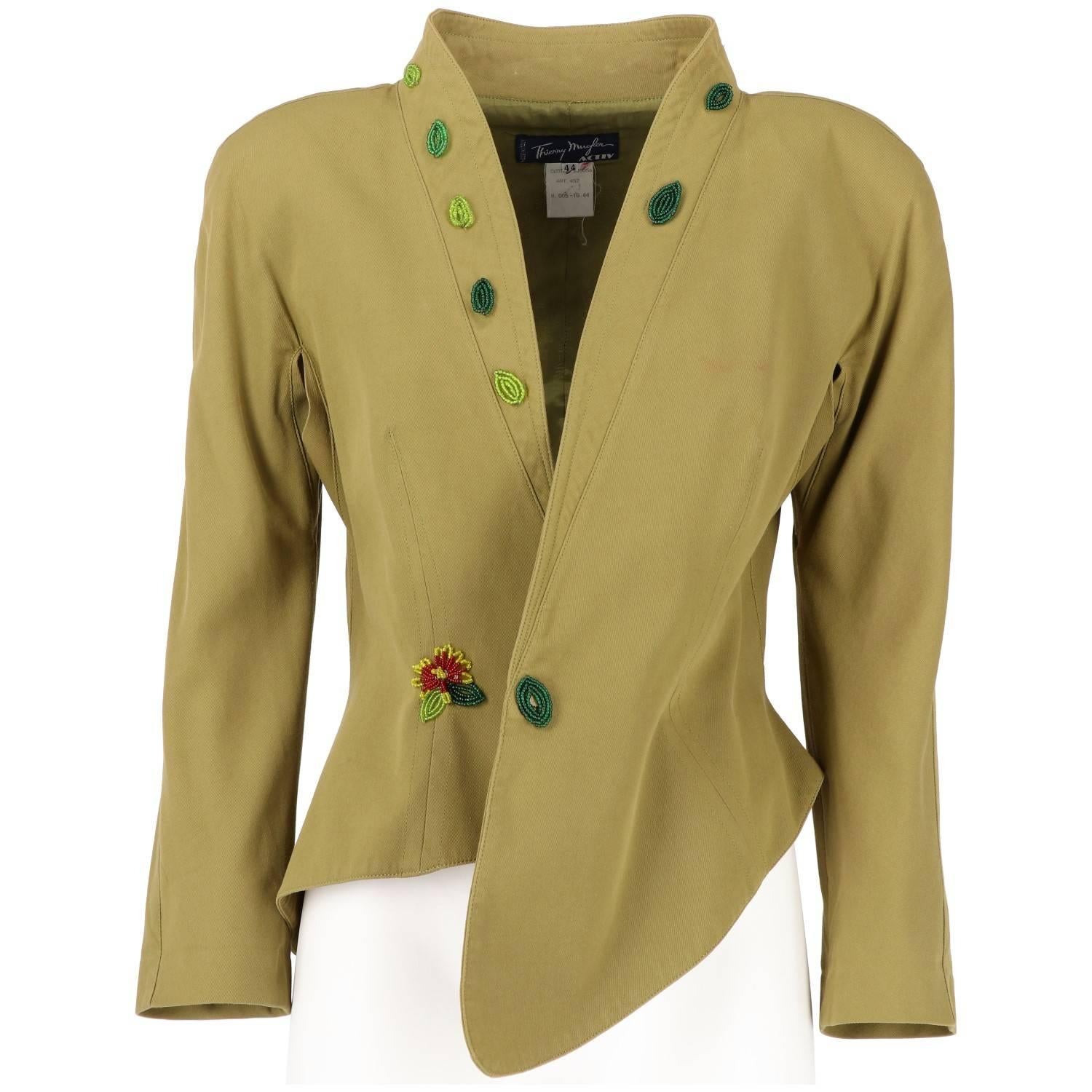 Thierry Mugler olive green cotton blazer jacket with beaded flowers and leaves appliqué. It features a peculiar asymmetrical shape, plunge collar, and button fastening. The main button is covered by beads and remains opened. The item is vintage, it