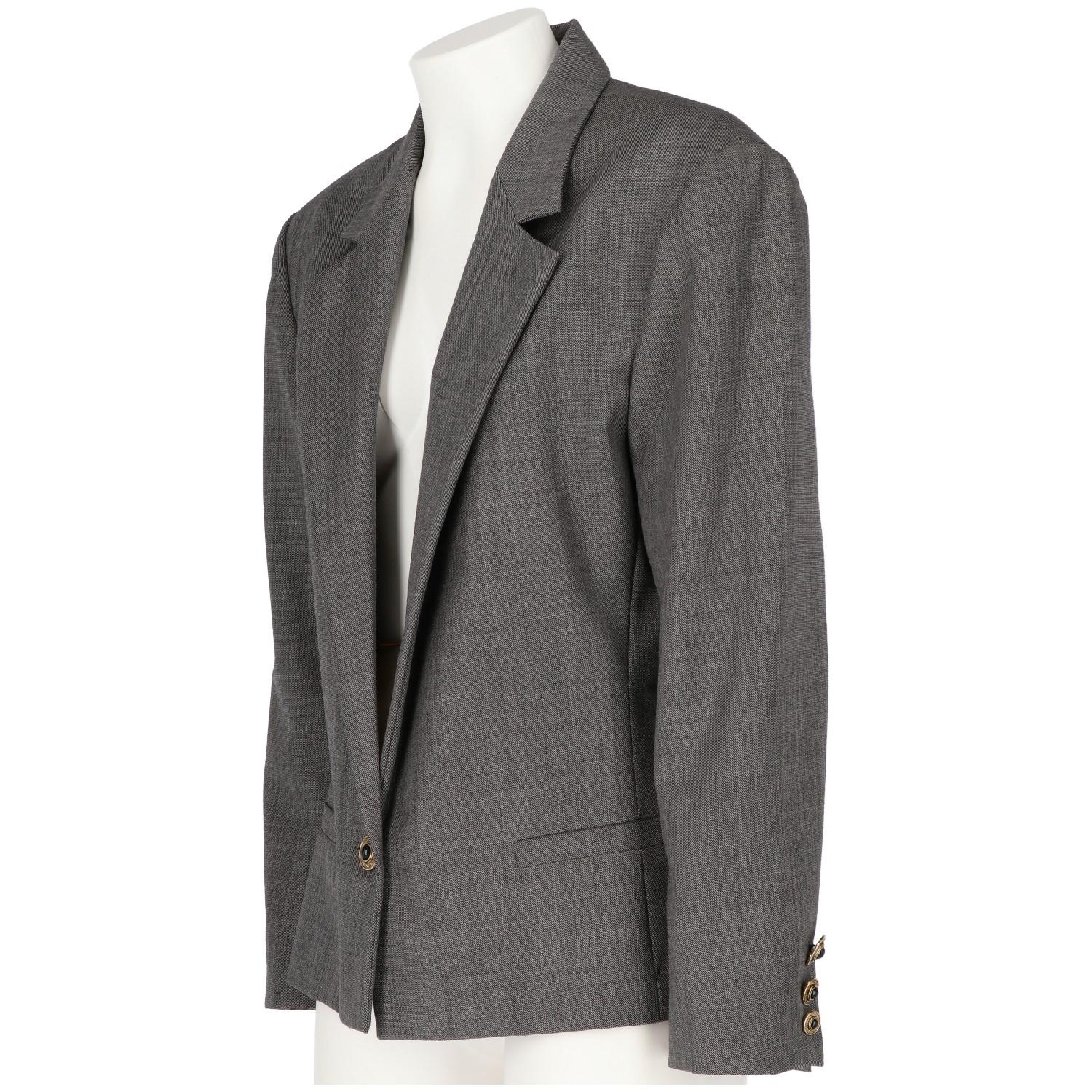 Classy grey virgin wool Versus jacket by Gianni Versace Vintage. It features a single decorated button fastening, peaked lapels, front welt pockets, long sleeves, button cuffs and a straight hem. The item is vintage, it was produced in the 80s and