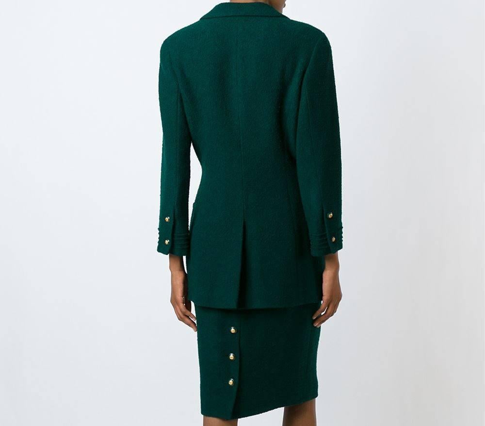 Classic Chanel silk and wool skirt suit in a dark green color. It features a blazer with notched lapels, long sleeves, button cuffs, a front button fastening, front pockets, a rear central vent and a straight fitted skirt with gold-tone rear