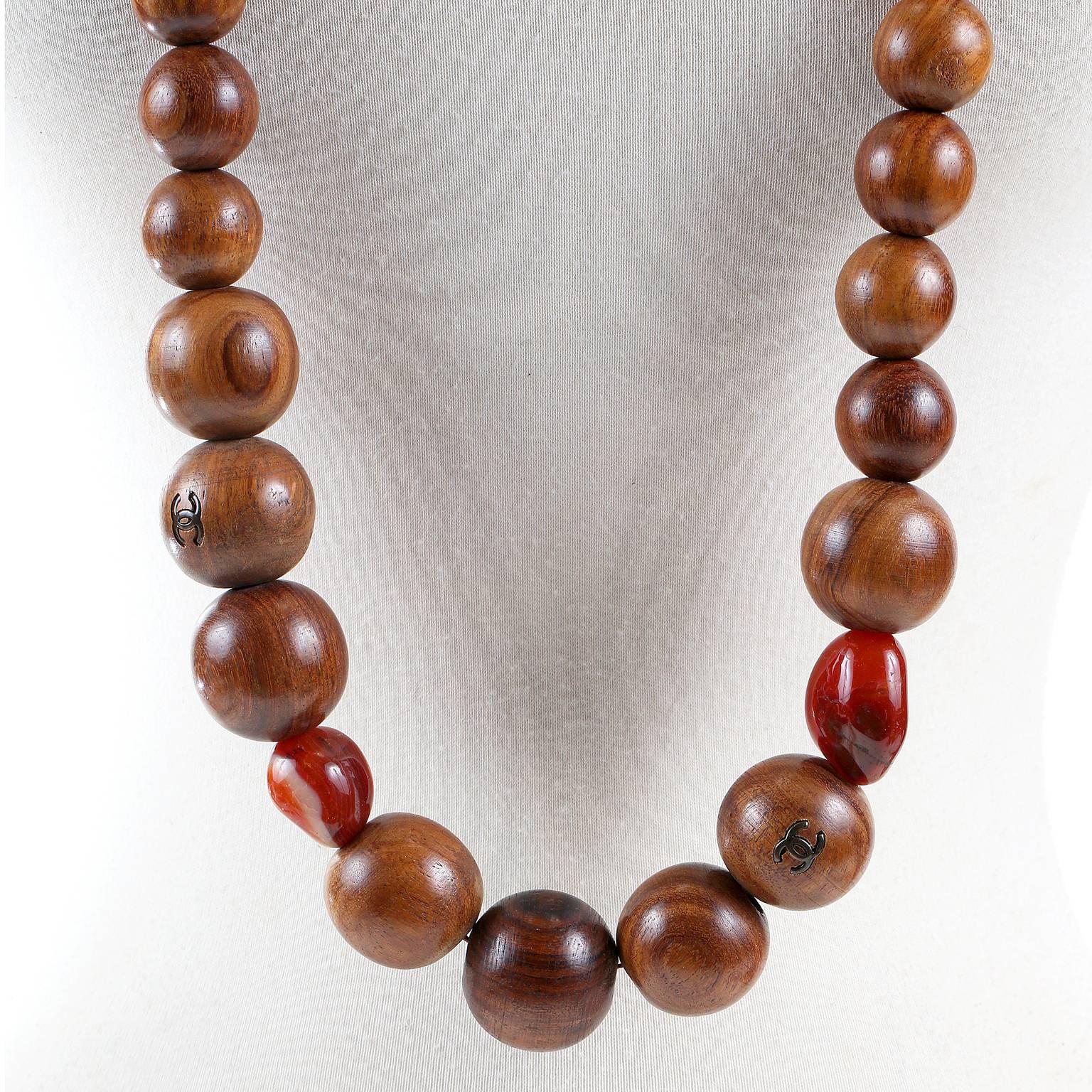 This authentic Chanel Wooden Bead Long Necklace is in pristine condition.  
Large dark brown wood beads interspersed with red toned irregularly shaped stones.  Interlocking CC’s are on several of the beads.  Circa 1980’s.  
A225
