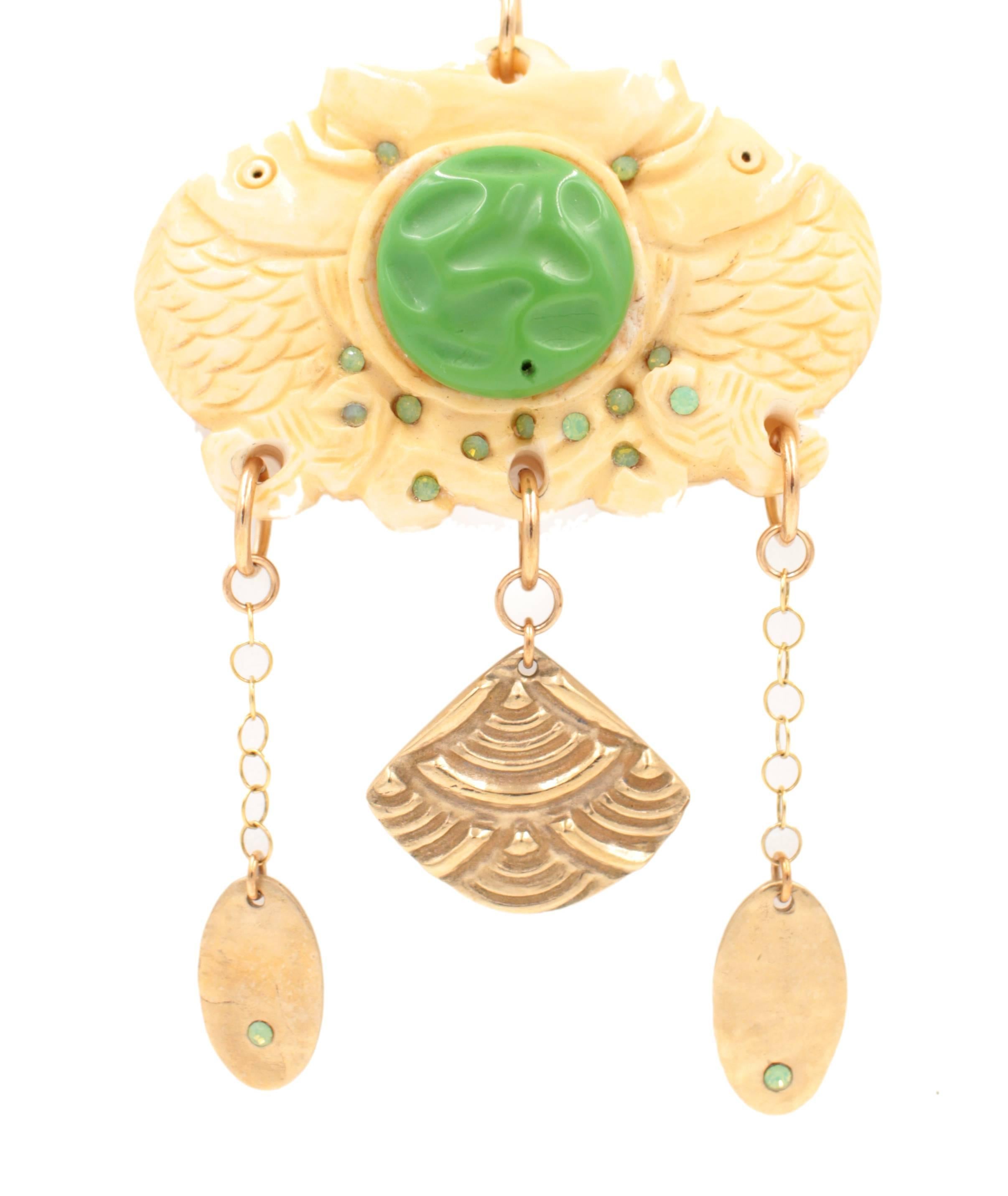 The Double Fish Pendant Necklace features a carved bone double fish with a delightful vintage green glass center set with vintage Swarovski Crystals accented by bronze clay dangles. The piece measures 26 x 2.5 in.