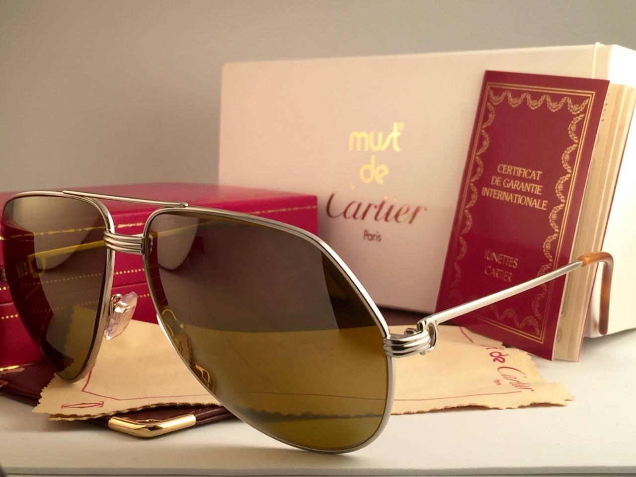 New Cartier Aviator Vendome in the ultra rare Platinum plated sunglasses with gold mirror (uv protection) lenses in a Full Cartier Set.
Frame is with the famous Vendome stripes on the front and on the sides.
All hallmarks. Honey brown enamel with