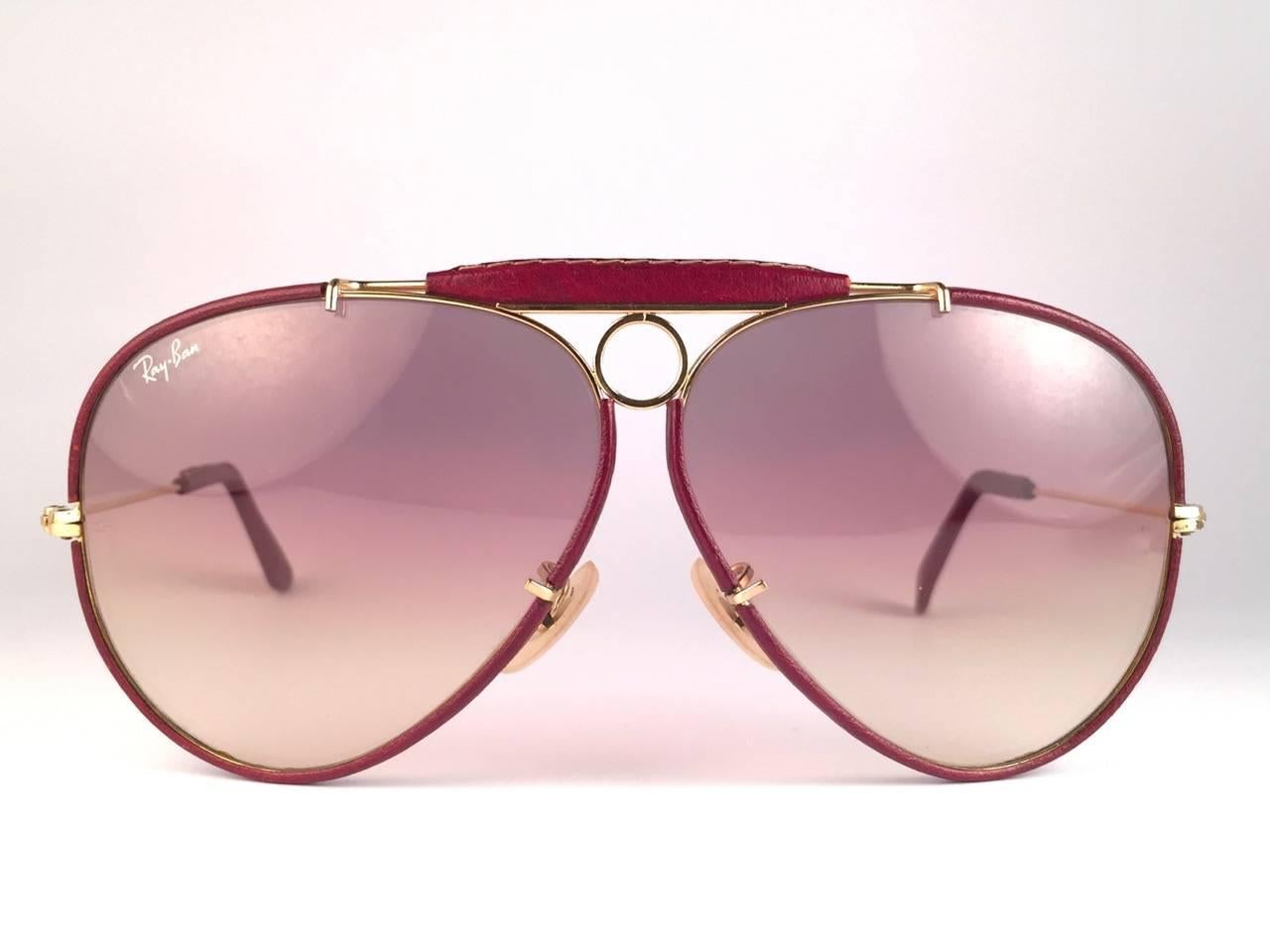 New Vintage Ray Ban Shooter 62 mm burgundy leather with rose gradient lenses with Ray Ban logo. 
B&L etched in the lenses, so mid 1970's. 
Comes with its original Ray Ban B&L case.
Rare and hard to find!