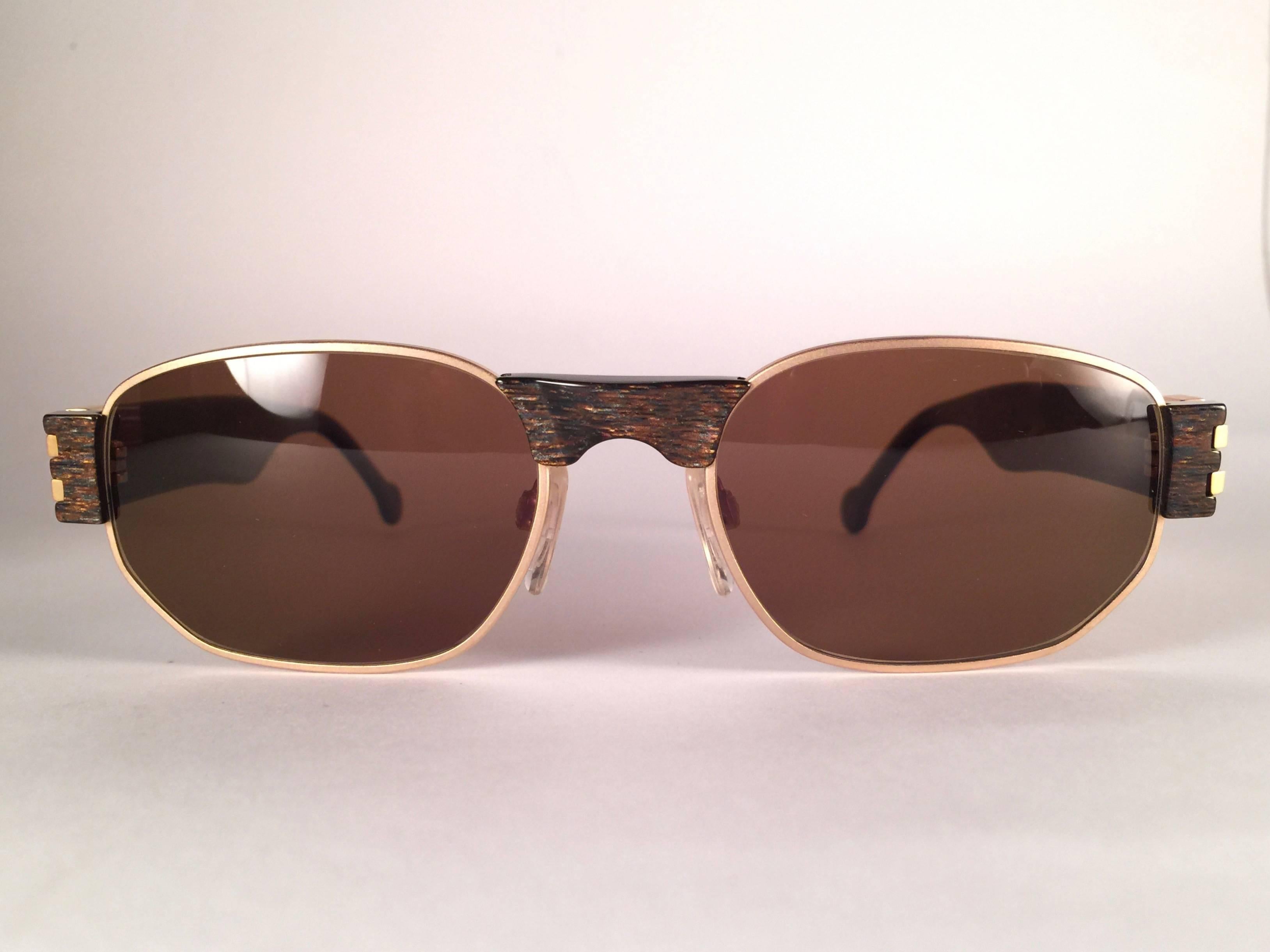 New, never worn Karl Lagerfeld matte gold with translucent stripes frame holding a spotless pair of solid brown lenses.  
Designed and produced in 1990's. 
New, never worn or displayed.
Made in Austria.