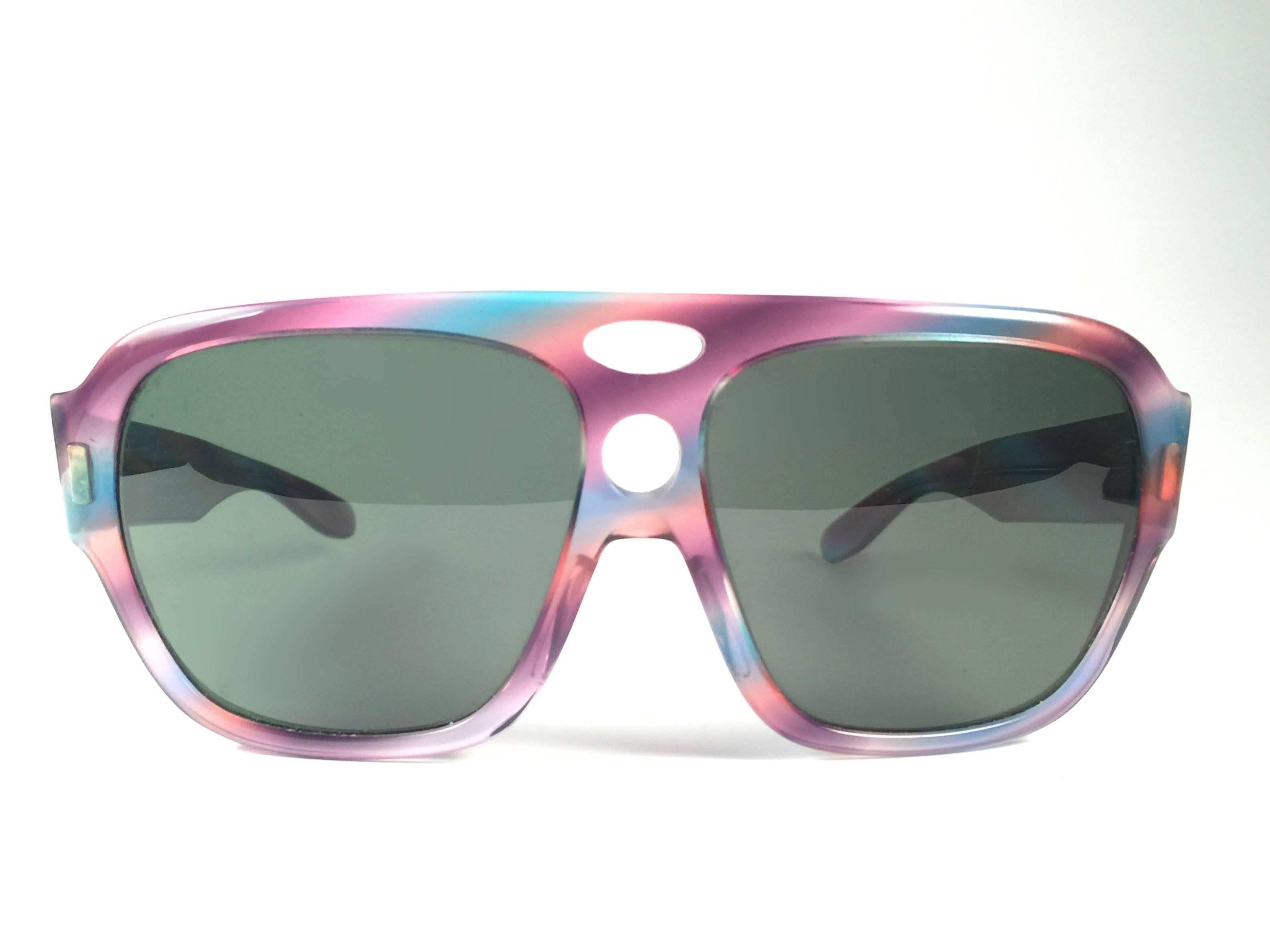 New and rare Vintage Corrigan II multicolor frame holding a spotless pair of G15 grey lenses.  
New, never worn or displayed.  
This pair may have minor sign of wear due to nearly 40 years of storage, the lens have two small scratches not on the