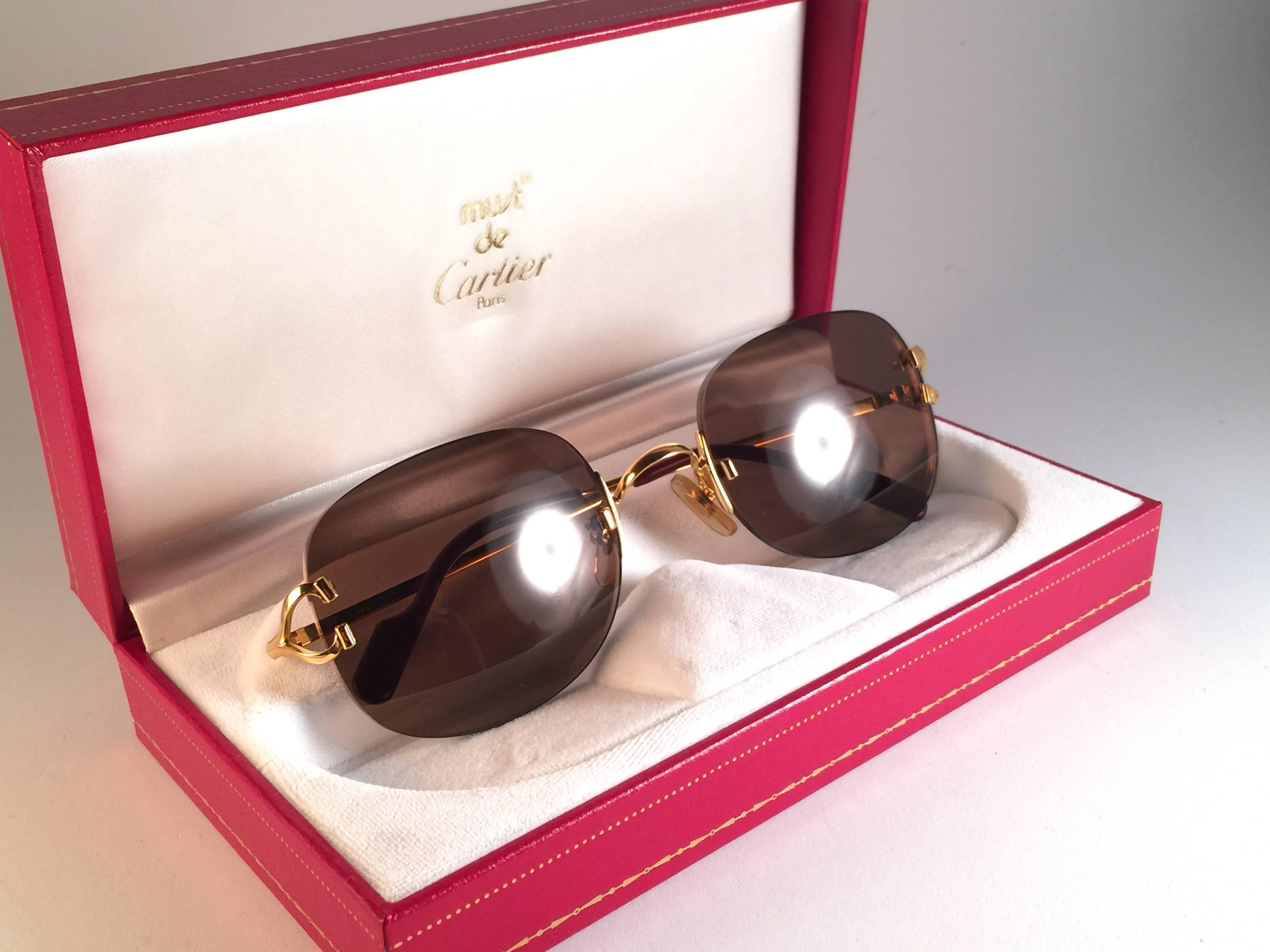 New Cartier Serrano unique rimless sunglasses with brown cartier (uv protection) lenses.  Frame with the front and sides in gold. All hallmarks. Cartier gold signs on the black ear paddles.  These are like a pair of jewels on your nose.  Beautiful