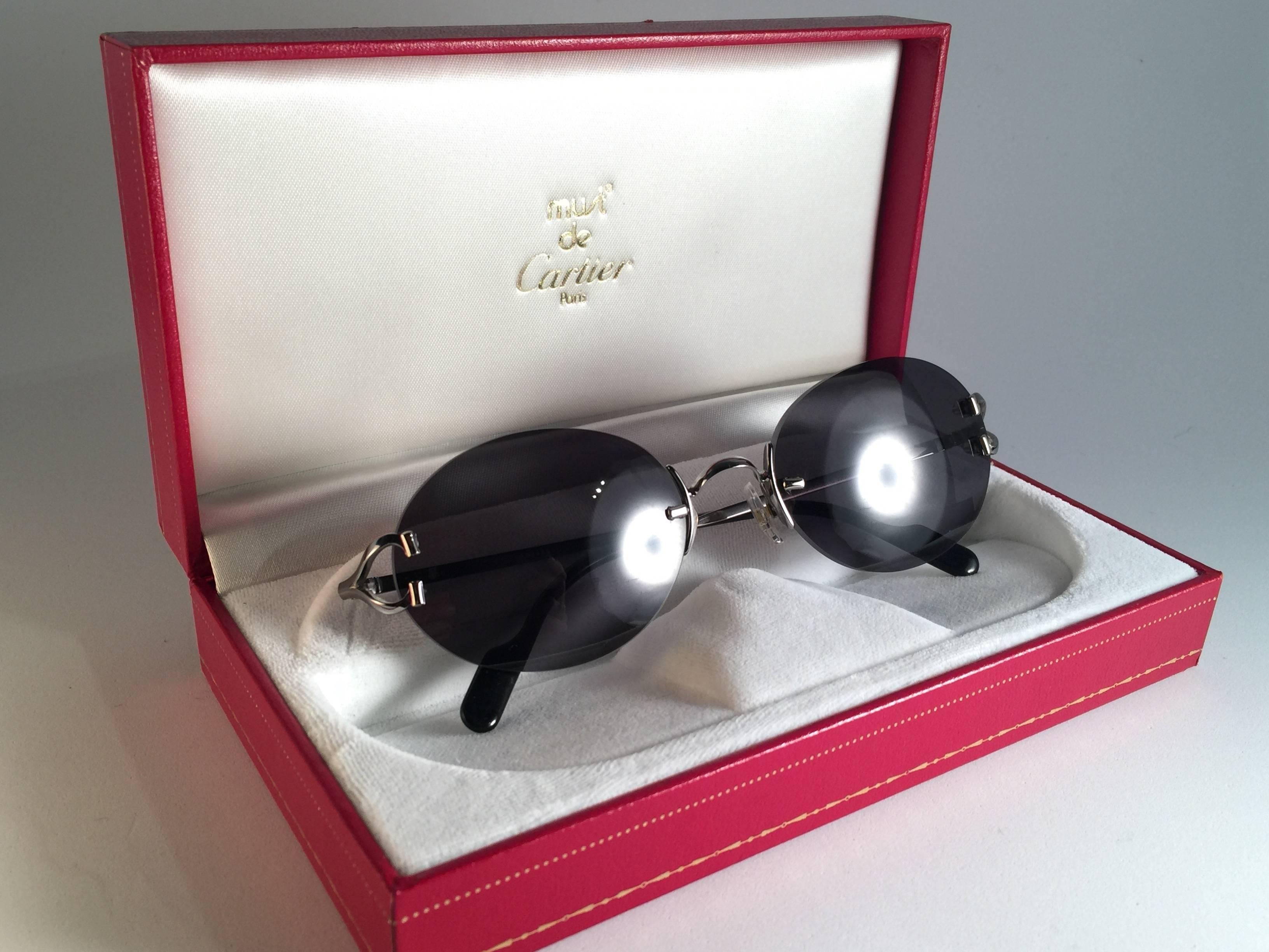 New 1990 Cartier Scala unique rimless sunglasses with grey (uv protection) lenses. Frame with the front and sides in plating. All hallmarks. 

Cartier gold signs on the black ear paddles. 

Please notice this item its nearly 30 years old and may