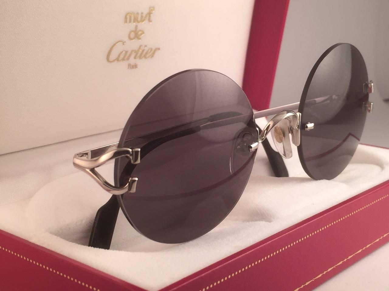 New 1990 Cartier Madison unique rimless sunglasses with grey (uv protection) lenses. 
Frame with the front and sides in Platine. 
Cartier Platine signs on the onyx black ear paddles. 
These are like a pair of jewels on your nose. 
Beautiful design