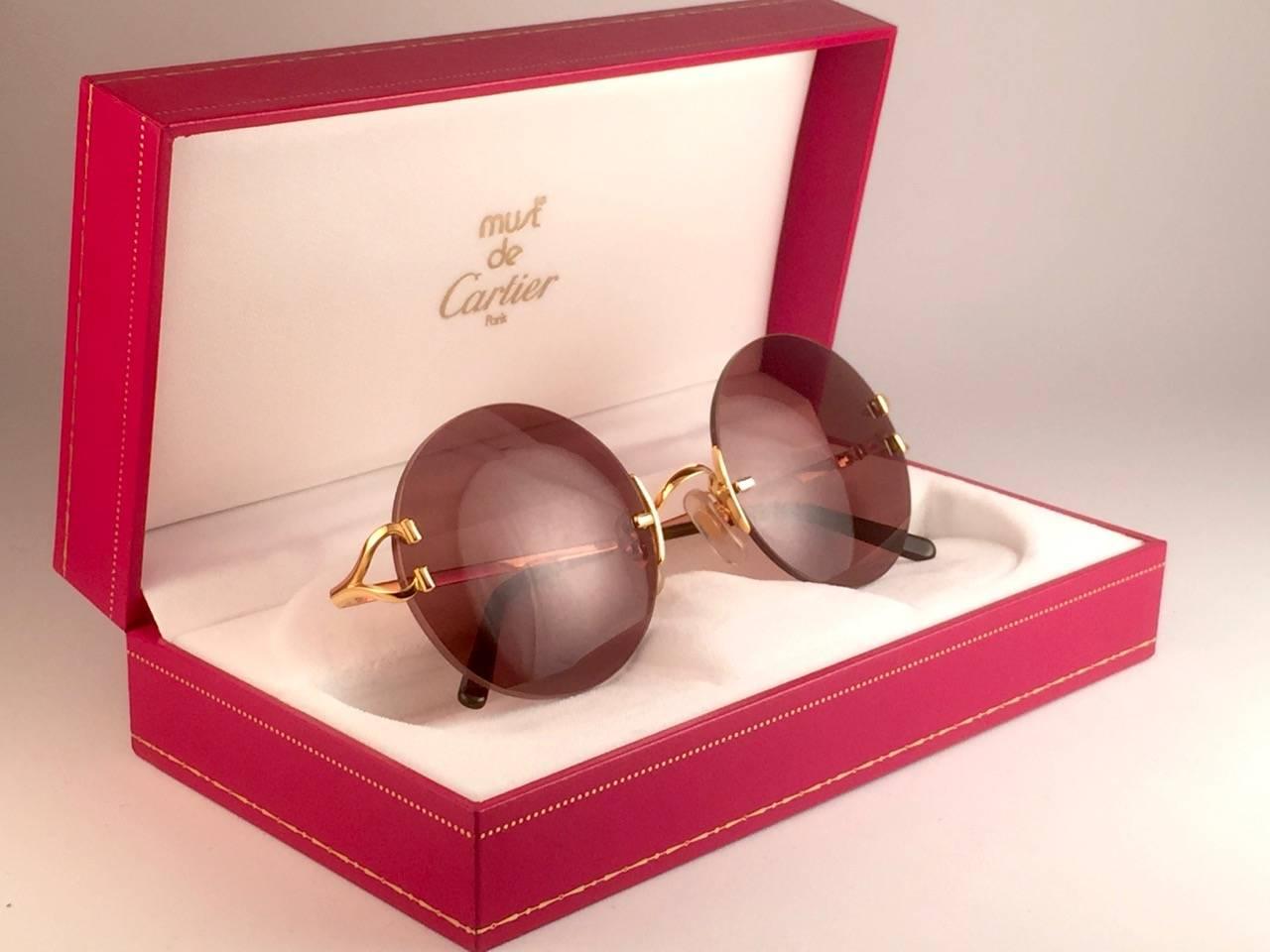 New Cartier Madison unique rimless sunglasses with brown  (uv protection) lenses. 
Frame with the front and sides in gold. All hallmarks. Cartier gold signs on the black ear paddles. 
These are like a pair of jewels on your nose. 
Beautiful design