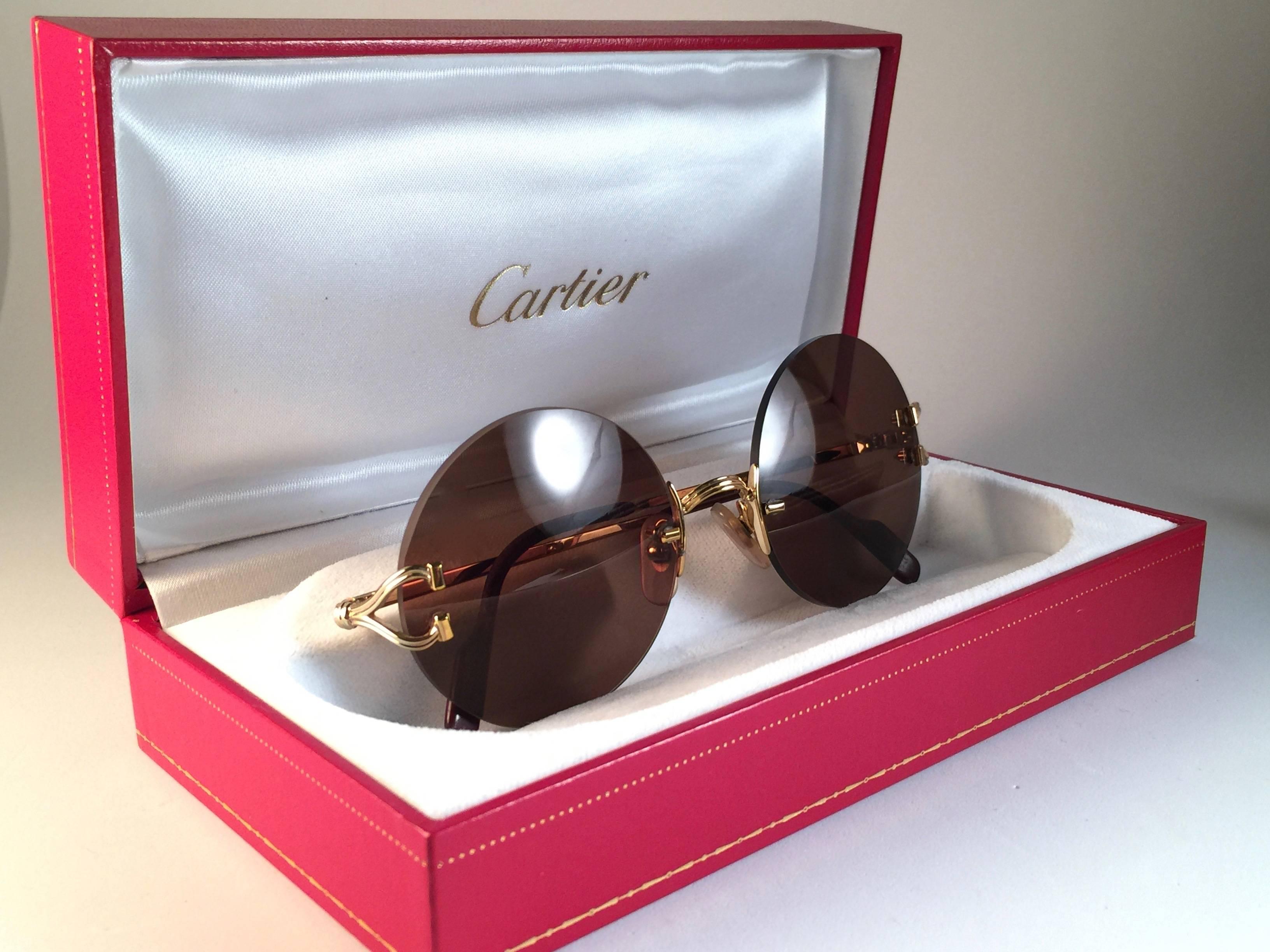 New Cartier Madison unique rimless sunglasses with brown Cartier (uv protection) lenses.  Frame with special details on the front and sides in gold. 
All hallmarks. Cartier gold signs on the black ear paddles.  
These are like a pair of jewels on
