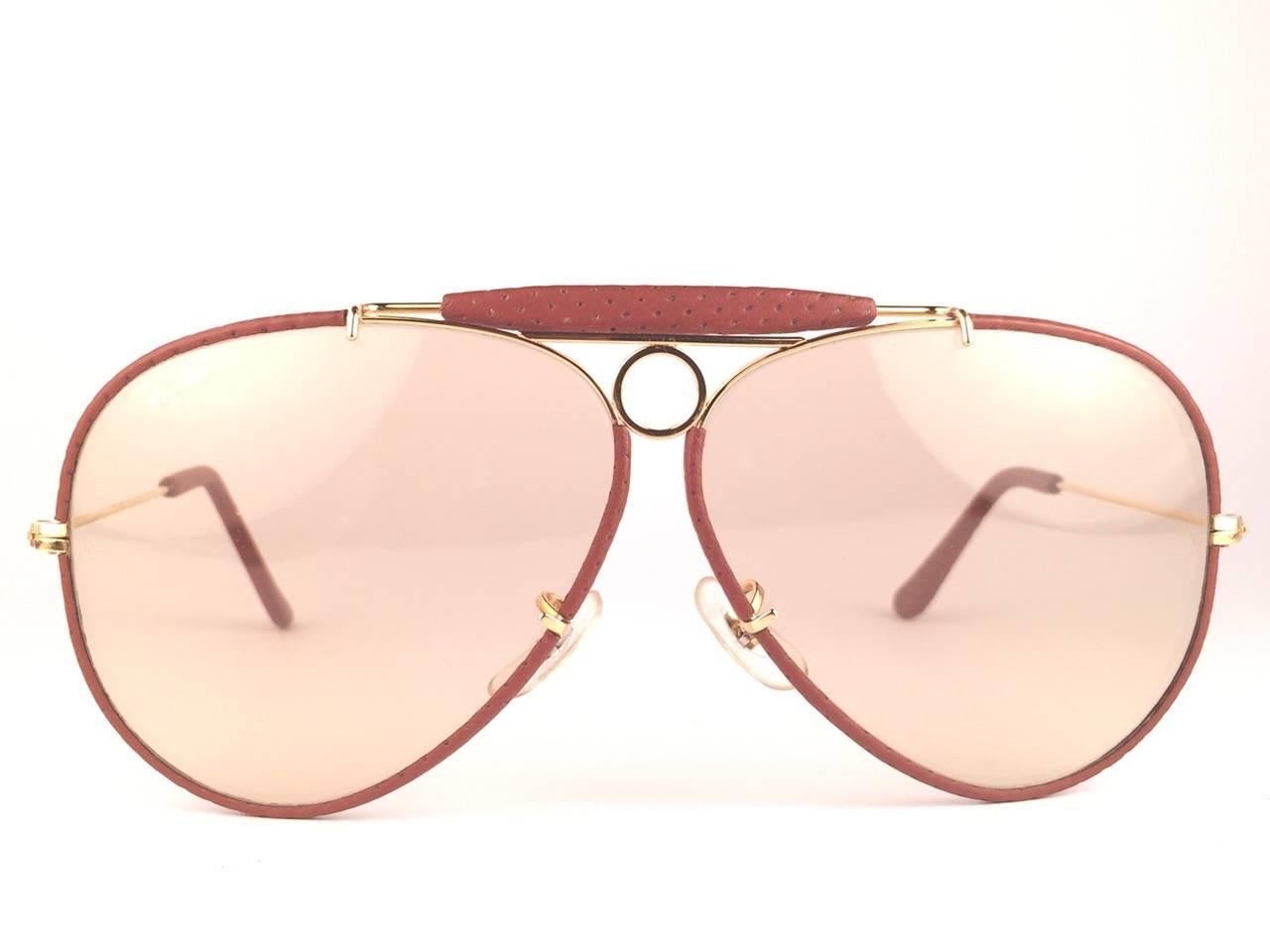 
New Vintage Ray Ban Shooter 62 mm in pelle di struzzo e metallo dorato con un paio di immacolate lenti intercambiabili marrone chiaro con logo Ray Ban. 

B&L inciso sulle lenti, quindi metà anni '70. 

Viene fornito con la sua custodia originale