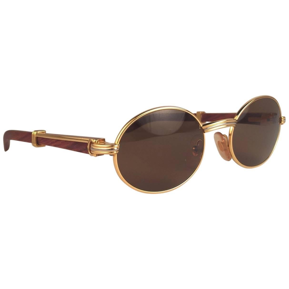 New Original Rare Yellow and White Gold 1992 Cartier classy Sully Sunglasses with rosewood temples and honey brown spotless uv protection lenses.  
Frame with the front and sides in yellow gold.  
All hallmarks.  Gold Cartier signs on the ear