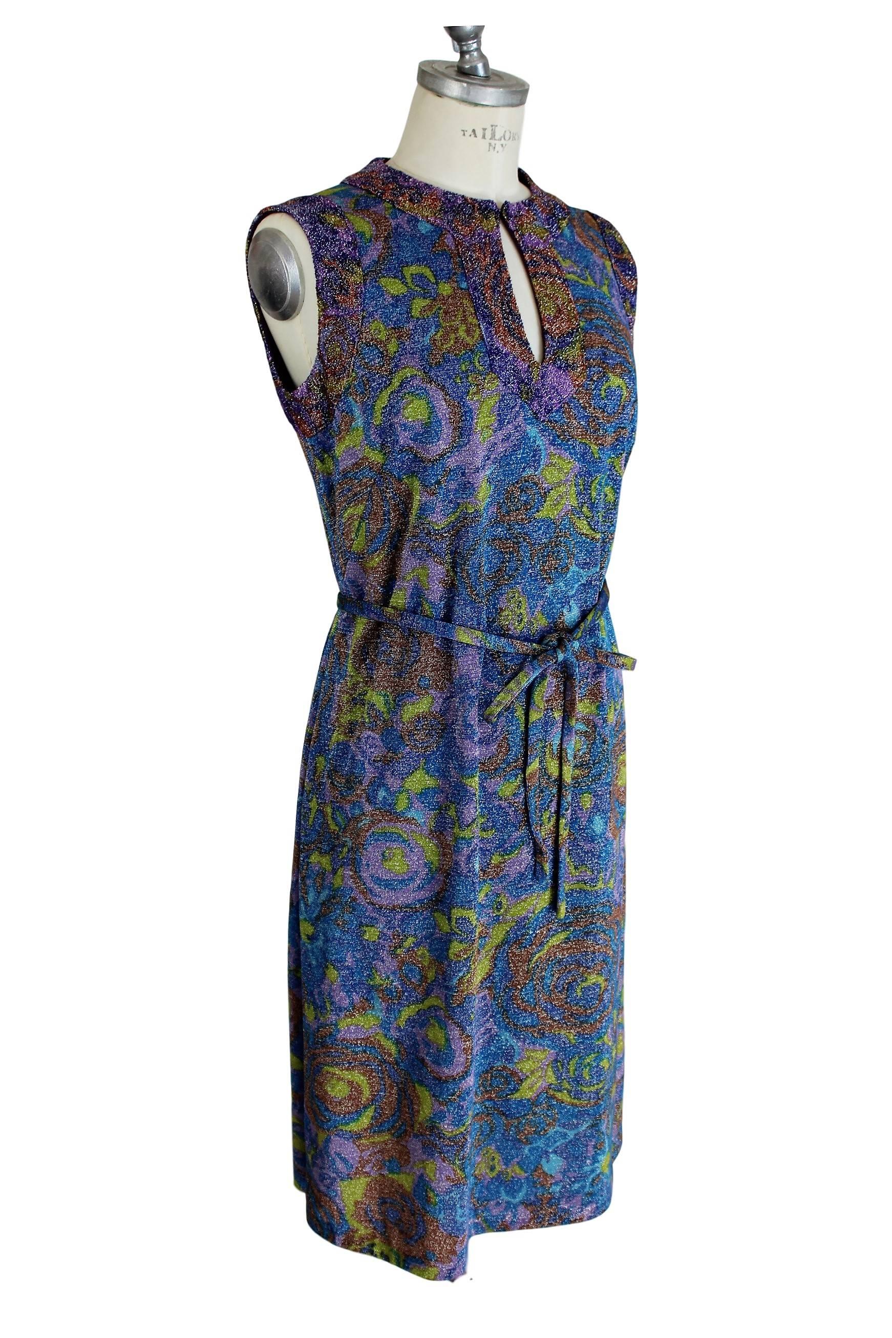 Rare tailored Sorelle Fontana Vintage 1960s dress gleaming metallic blue, floral motif. Neck closed by a flap open button on the chest. Belted waist.

Size: 42 (IT) / 36 (NL/DE) 

Measures: 

Shoulders: 42 cm 
Armpit to armpit: 48 cm 
Sleeves: no