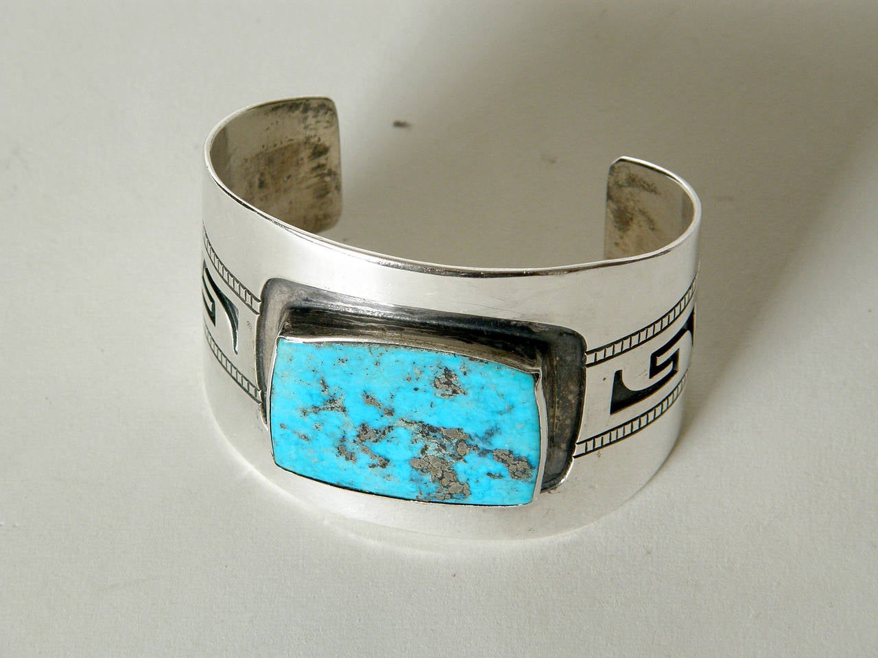 Handsome sterling silver cuff bracelet set with a large turquoise stone flanked by geometric designs reminiscent of a Greek key pattern, which I believe represents running water. Though this piece is unmarked, the original owner identified it as