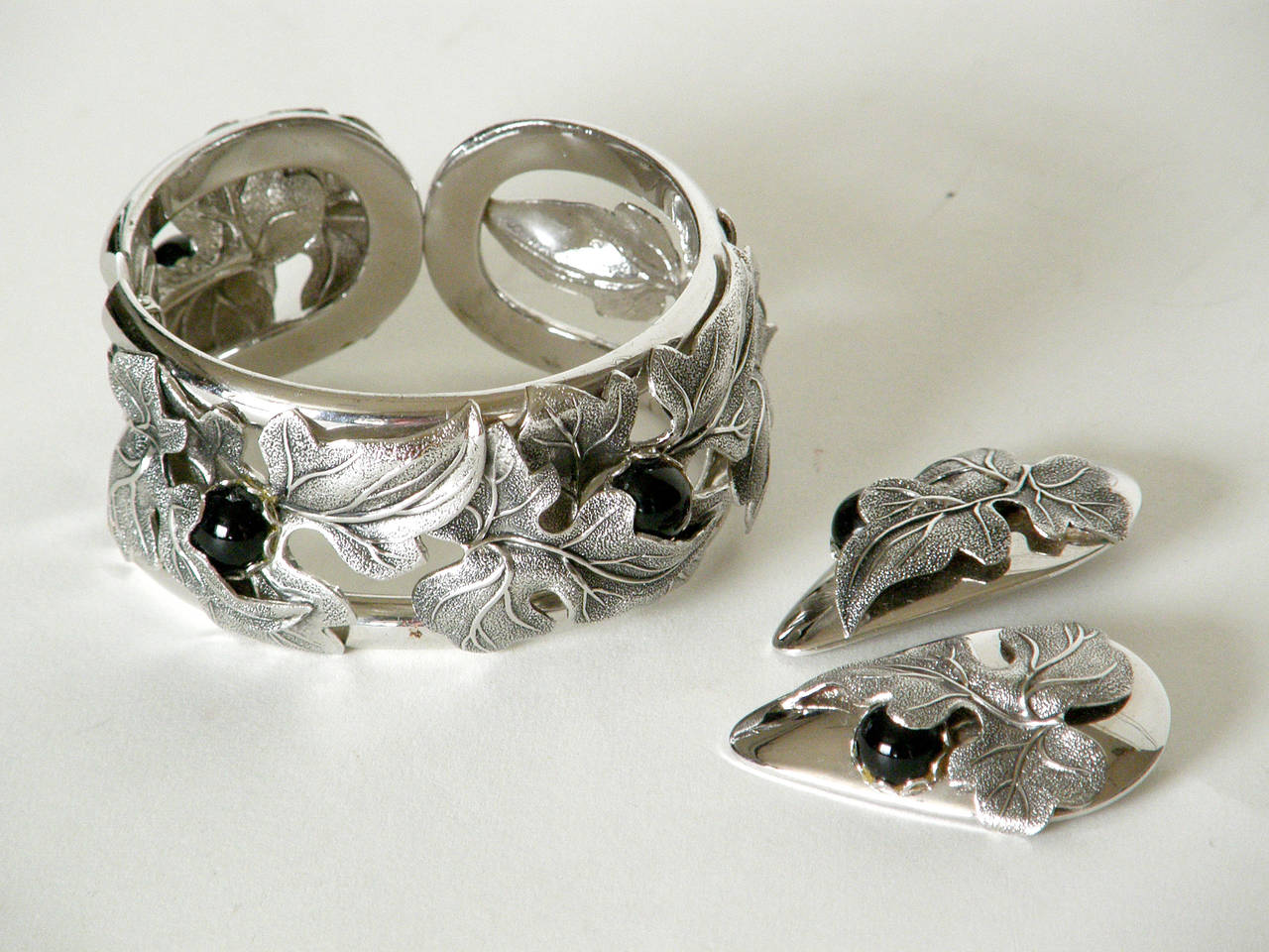 Whiting & Davis hinged cuff bracelet and earrings set with overlapping leaves and black cabochon stones.

approximate measurements:
bracelet- 1.25" w X 2.63" d x 2.38" h 
earrings- 1.13" w x 1.75" h x .5"