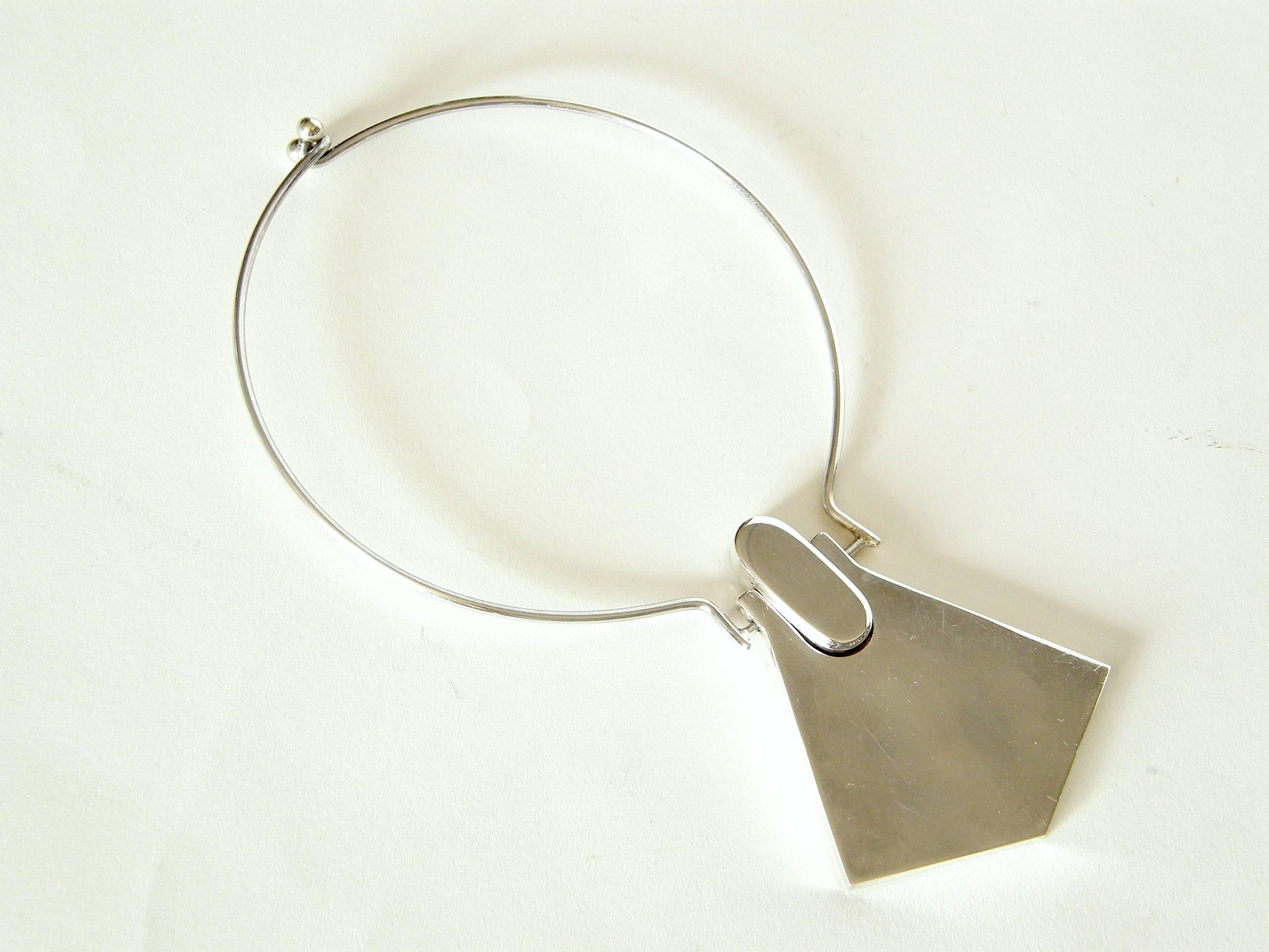 This sterling neck ring with integrated geometric pendant has a space age style. The two part pendant has a nice dimensionality, as the oval part at the top is deeper than the flared, angled part below it. 

Please contact us if you have any