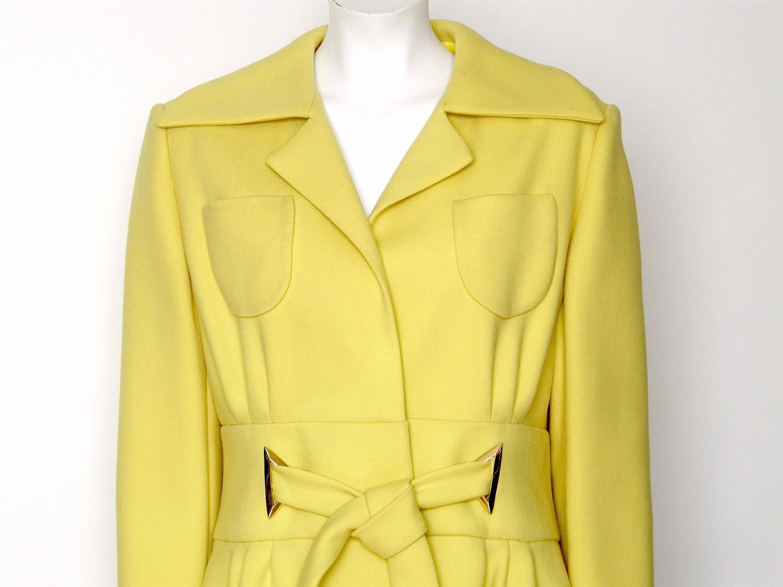 This sunny yellow coat will brighten up your winter days. It has a wide, splayed collar, 2 open top breast pockets, a wide waistband, and ties at the waist. There are stylish, gold-plated triangular accents where the ties attach to the waistband,