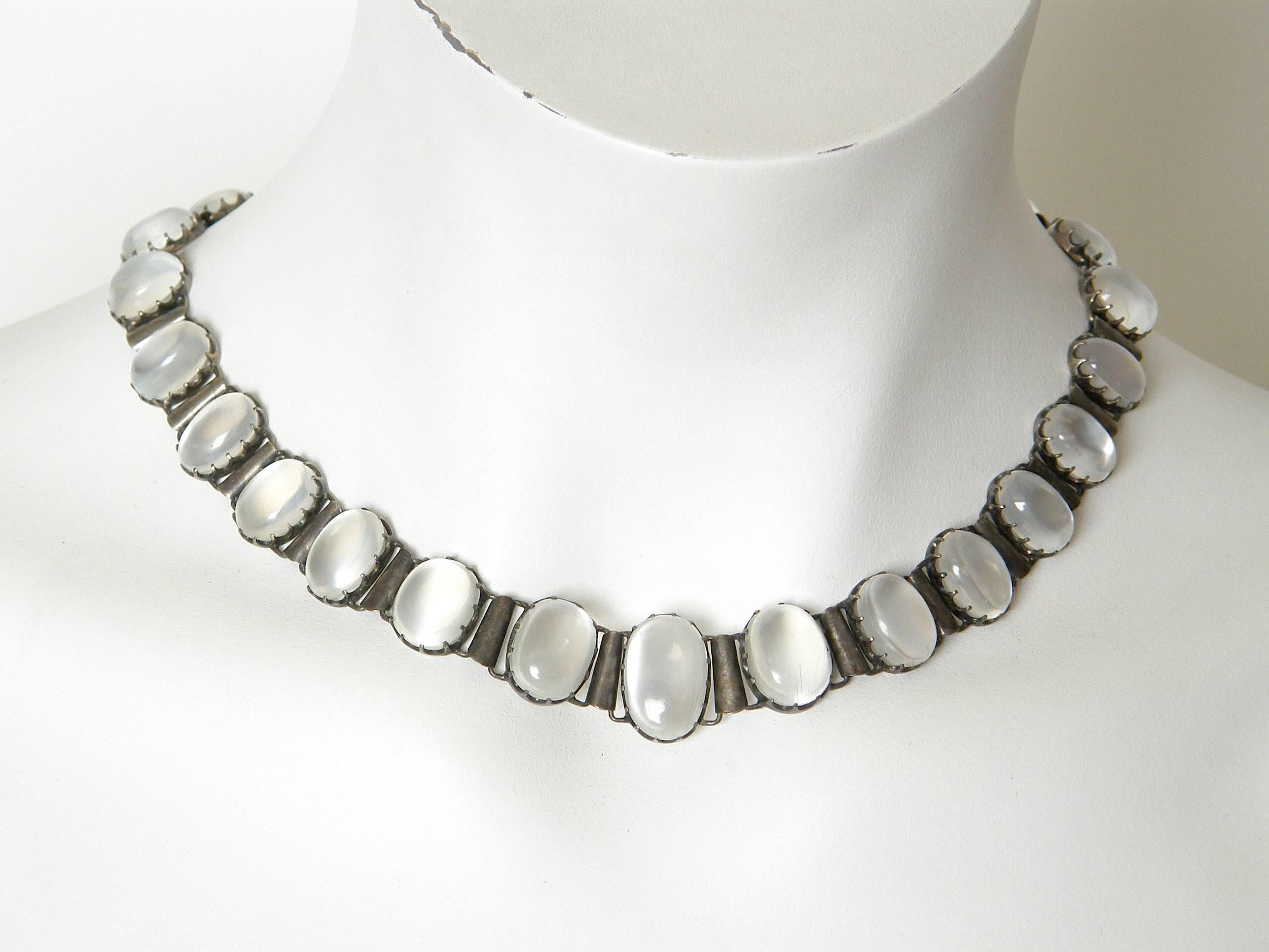 This ethereal choker necklace features 26 cabochon moonstones of varying sizes. The stones are held in place by multiple prongs, with a scalloped effect to the settings. The necklace is unmarked, but it tests for sterling. 

Please contact us if you