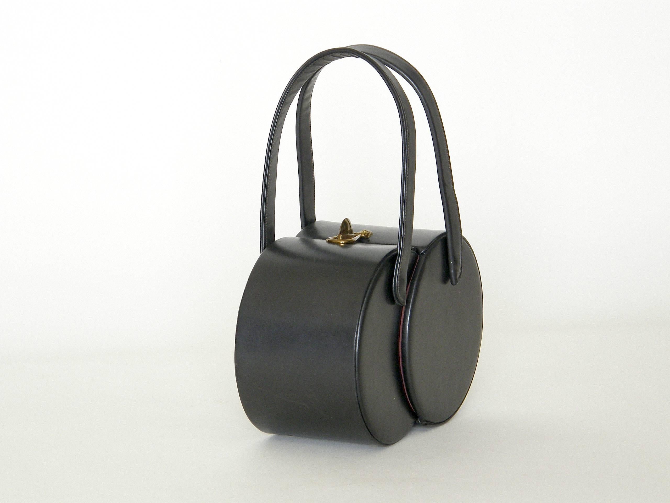This sculptural, graphite leather handbag is a fun twist on the box bag. It's made of two cylinders that overlap and pivot out to open. It has two top handles, a turn lock clasp and four little cap feet. The height is 5.5