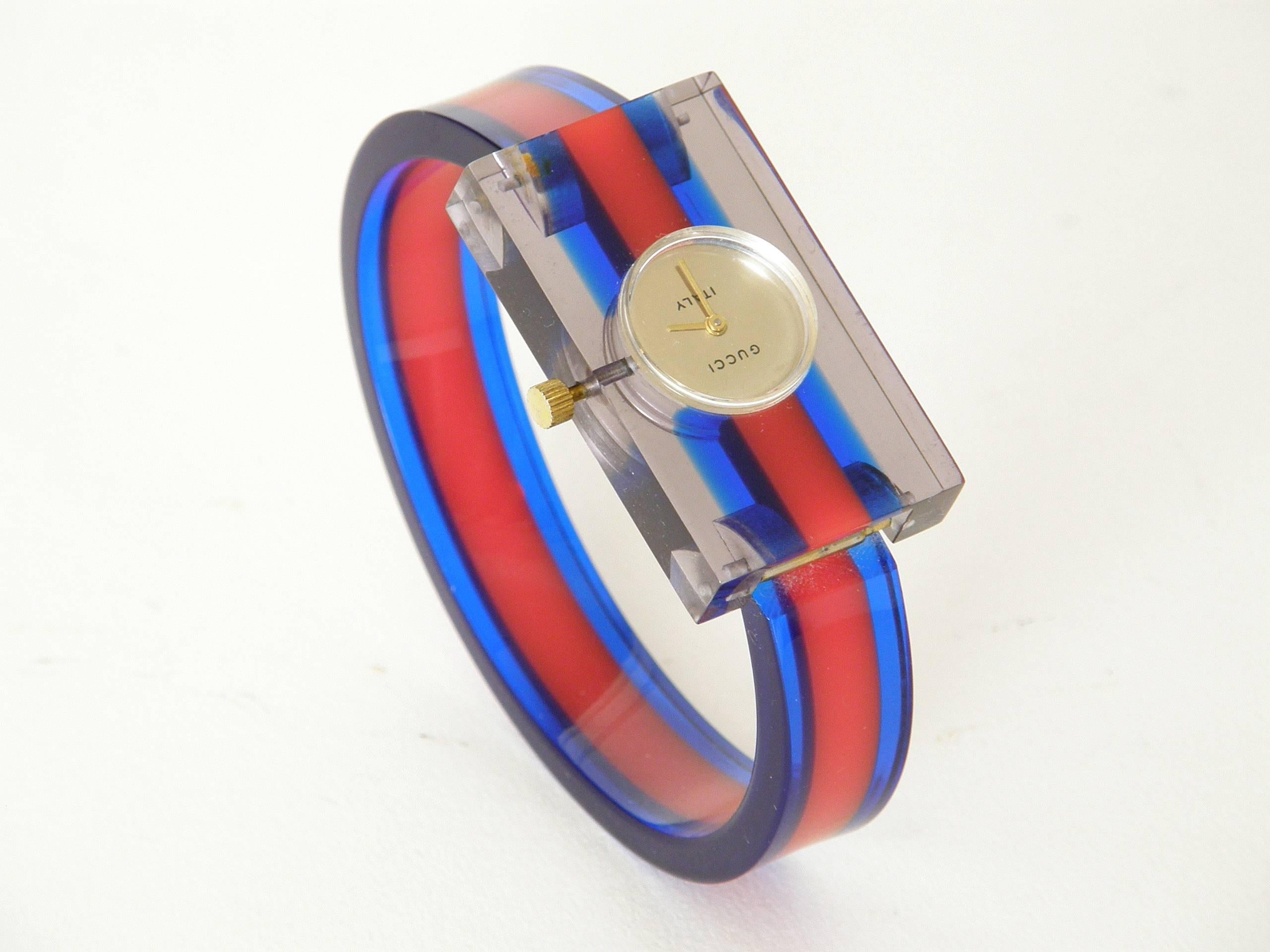 Colorful, striped lucite bracelet watch by Gucci. The rigid band is hinged to the rectangular face. It has a clear "skeleton" back which shows the inner workings of the watch. The light plays nicely through the lucite creating a luminous