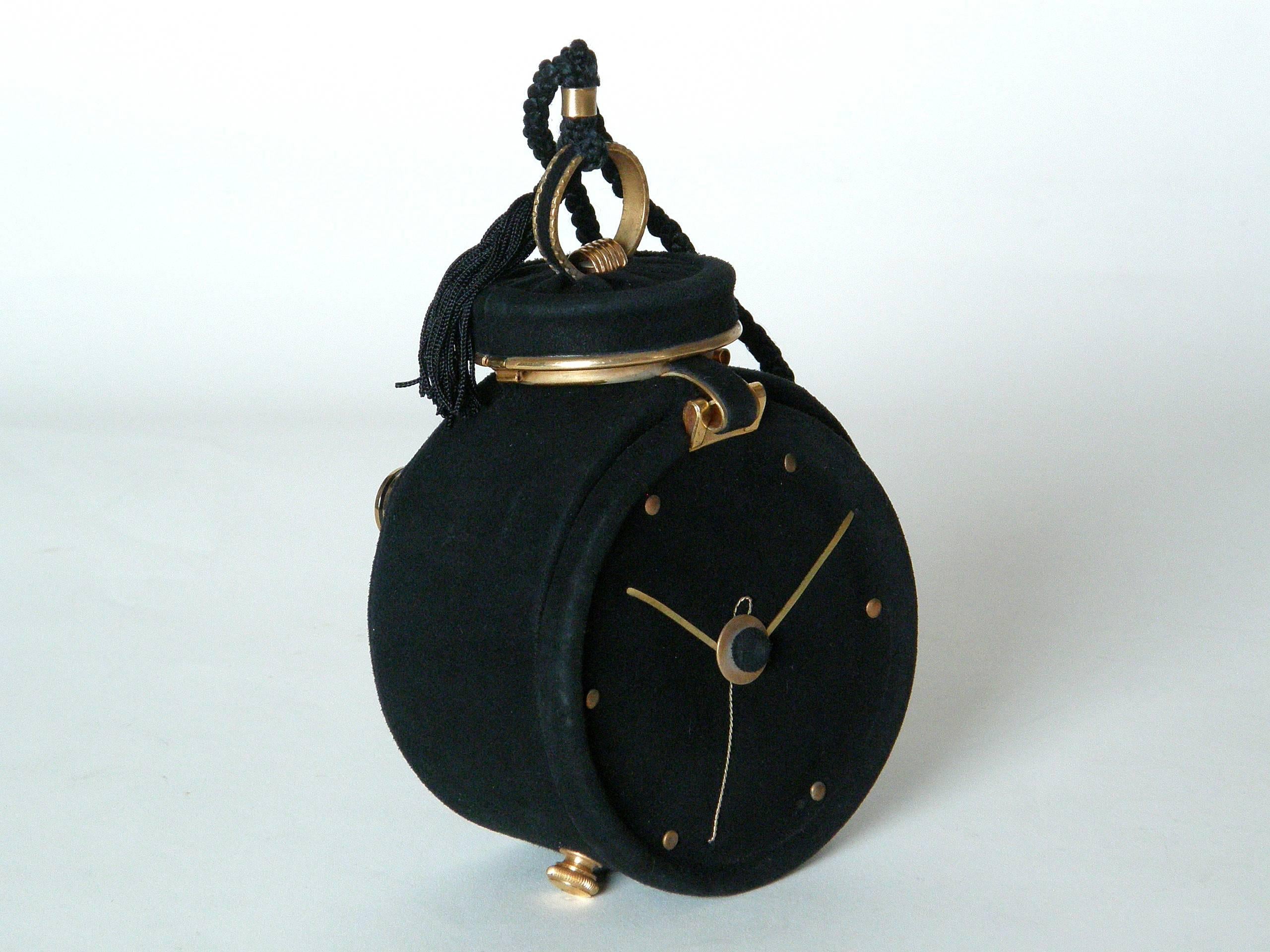 This marvelous figural handbag is shaped like an alarm clock. It's covered in a fine, black suede with details and accents in gold plated brass. The "bell" on top is a compact with mirror, and the "winding/time setting knob" on