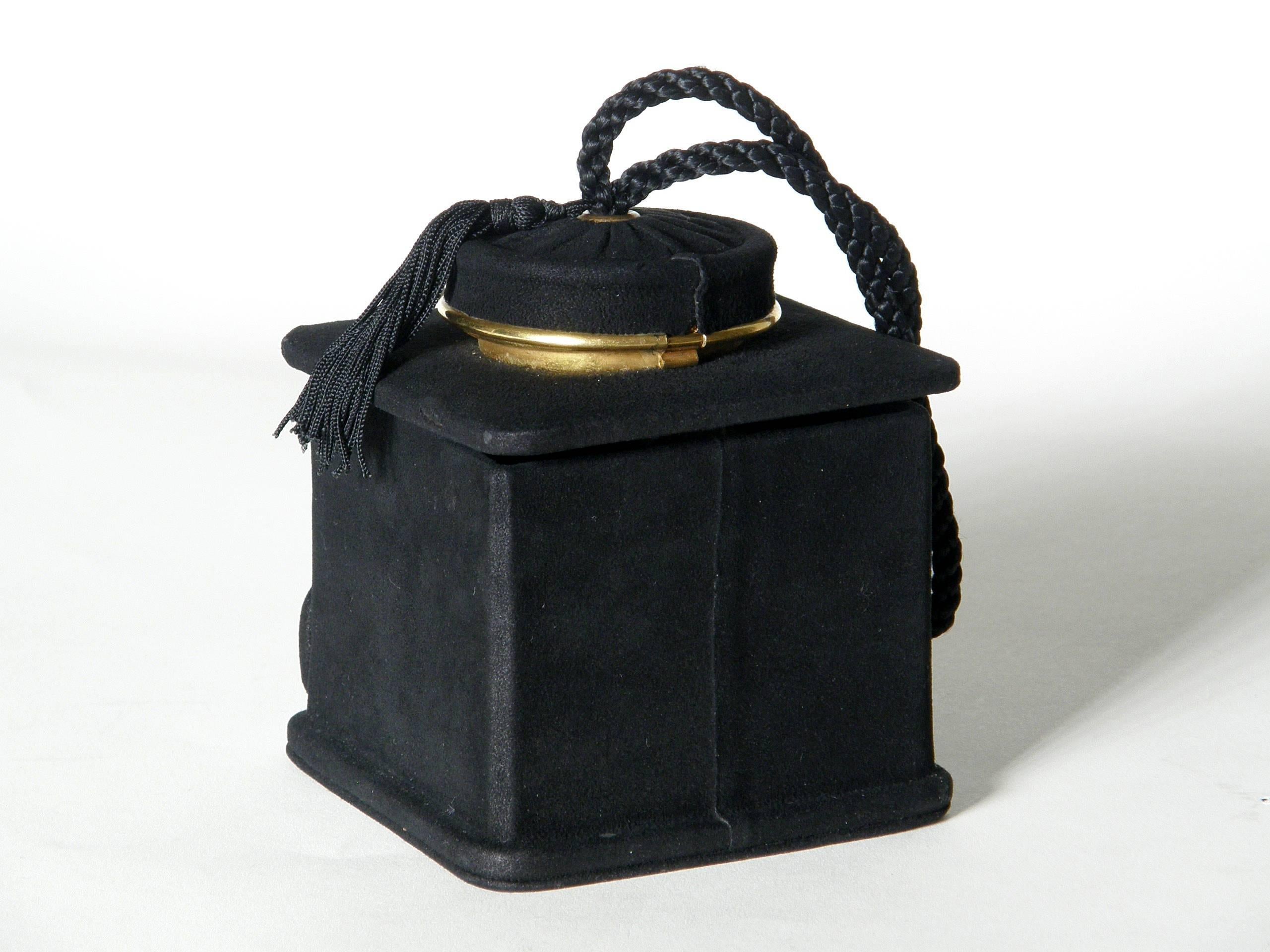 Ce charmant sac à main figuratif a la forme d'un moulin à café à l'ancienne. Il est recouvert d'un fin daim noir, avec des détails et des accents en laiton plaqué or. L'intérieur du couvercle qui s'ouvre pour accéder au corps principal du sac est