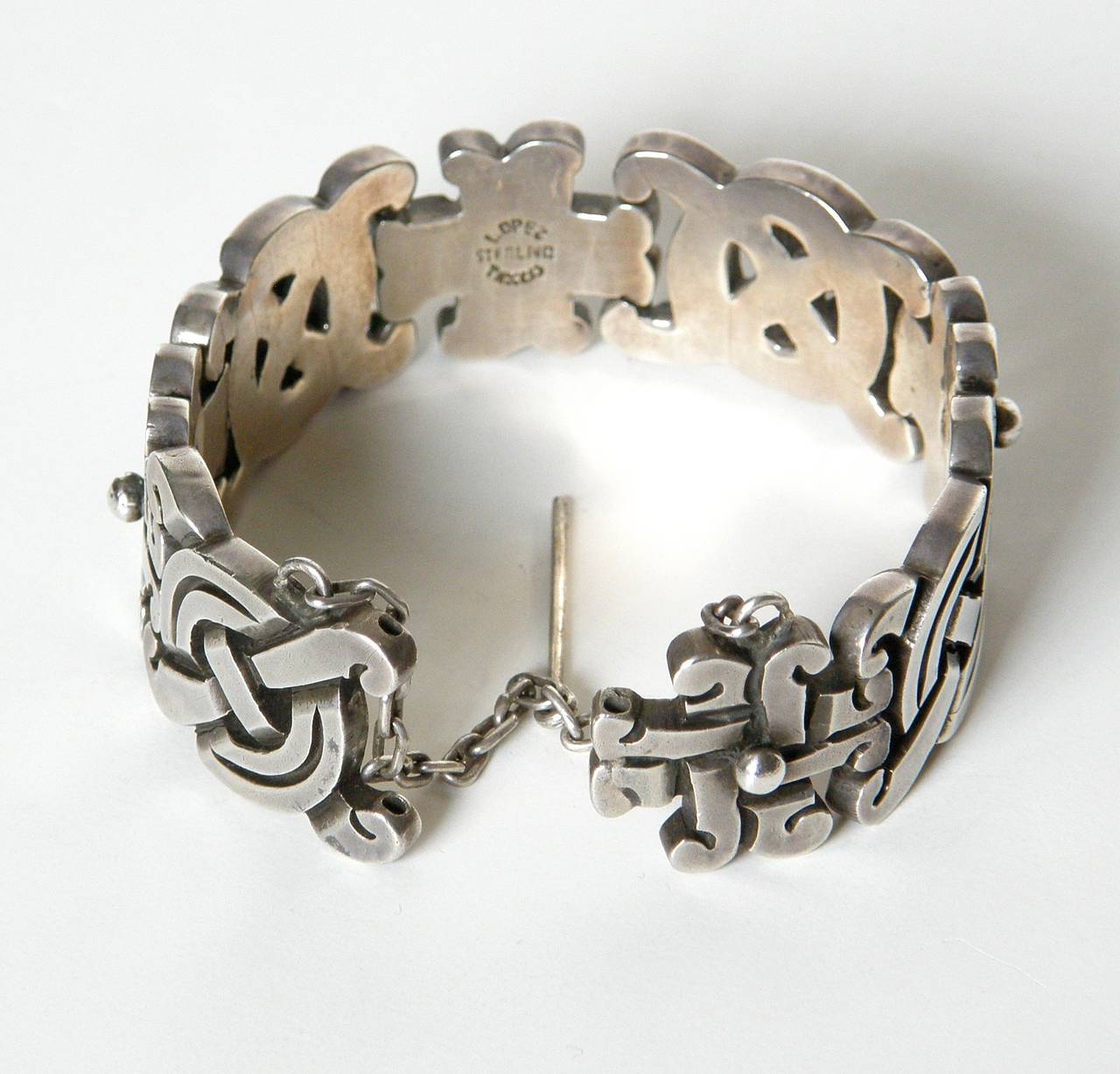 Heavy sterling link bracelet designed by Gerardo Lopez of Taxco, Mexico. The thick links have designs inspired by pre-Columbian motifs. The bracelet has a pin on a chain that slides through the two end links to form a closure. It has a nice vintage