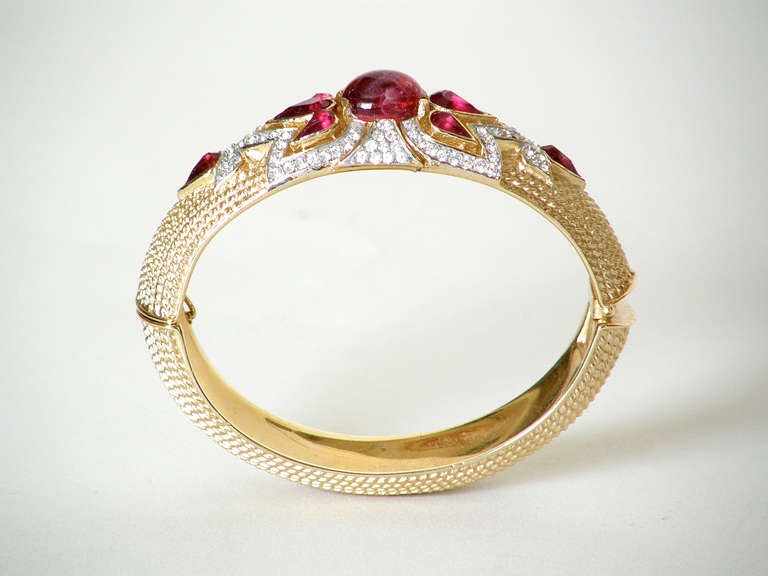 Elegant, hinged bangle bracelet designed by Alfred Philippe for the 1965 "Jewels of India" collection by Trifari. The textured gold bangle is oval shaped and set with faux diamonds and rubies in a classic Moghul style design.

bracelet