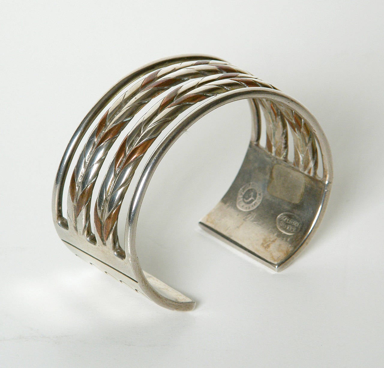This handsome William Spratling bracelet has two braided or twisted bands made up of thick sterling and copper stock flanked by two plain sterling bands. They terminate at rectangular sterling sections with incised lines and circles. It has a nice