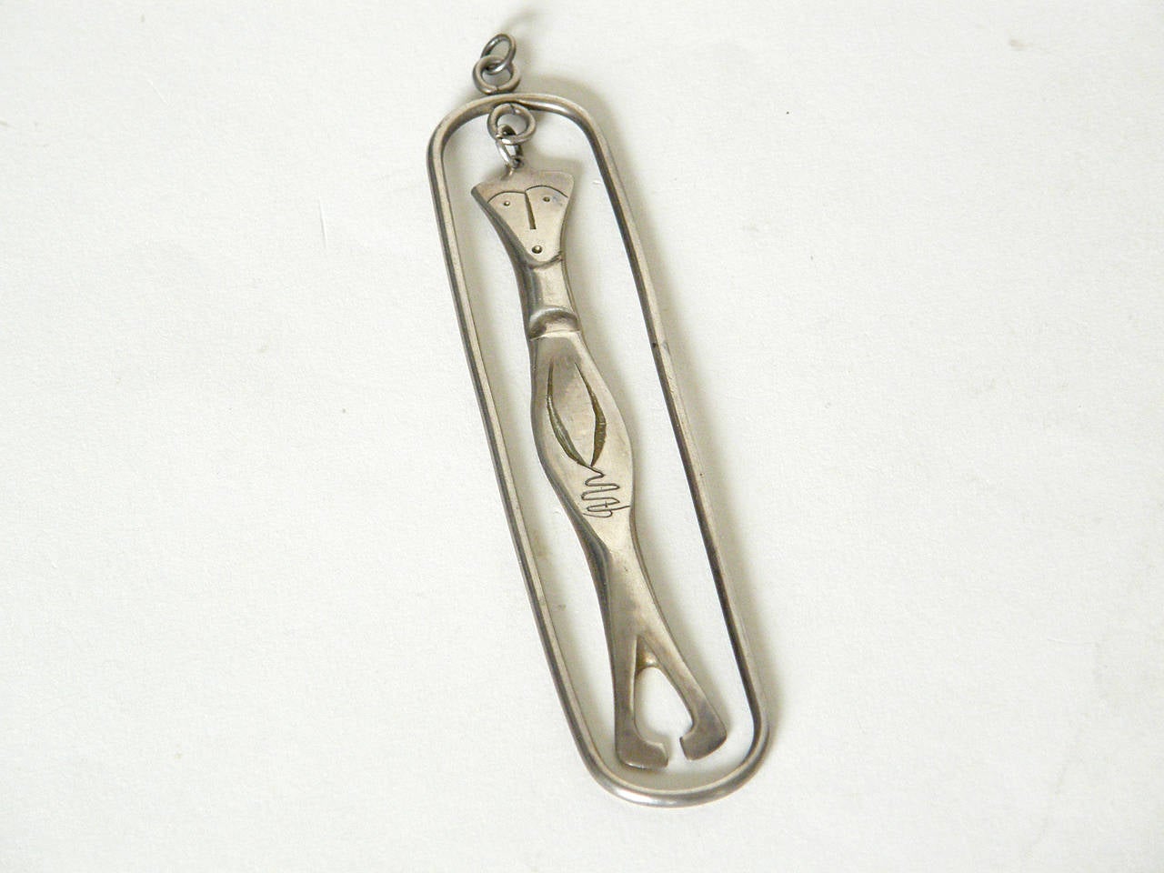 This sterling pendant of a man with his hands clasped hanging inside a silver frame was made by the husband and wife jewelers Irvin and Bonnie Burkee. It has a playful, modernist style typical of their work from the mid-20th century.

Please
