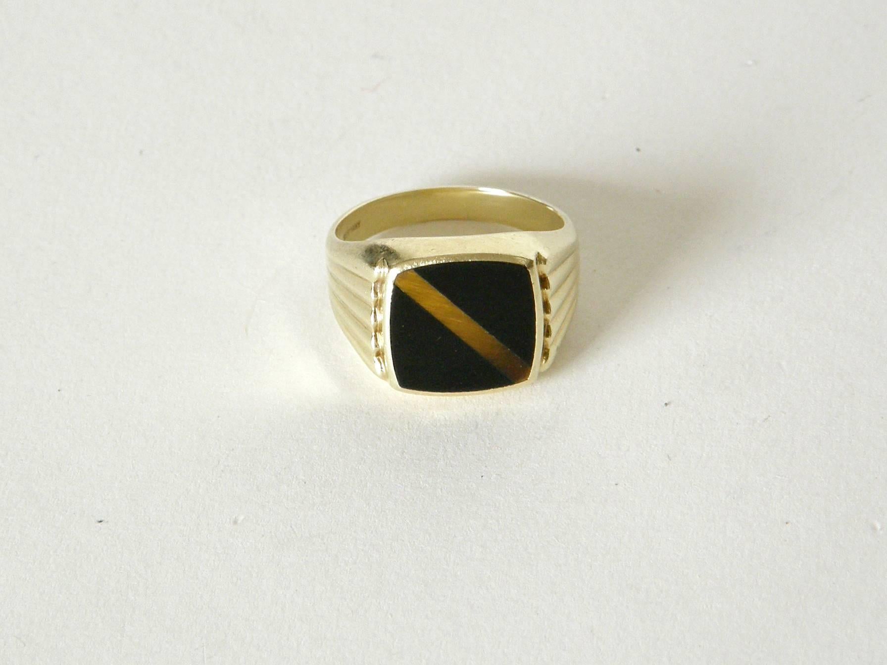 Handsome 14K yellow gold signet style ring. It has a flat bezel set with onyx and tigers eye and fan snapped designs on the sides. The technique of the stone setting is like a pieta dura with tight, flush edges between the onyx sides and the