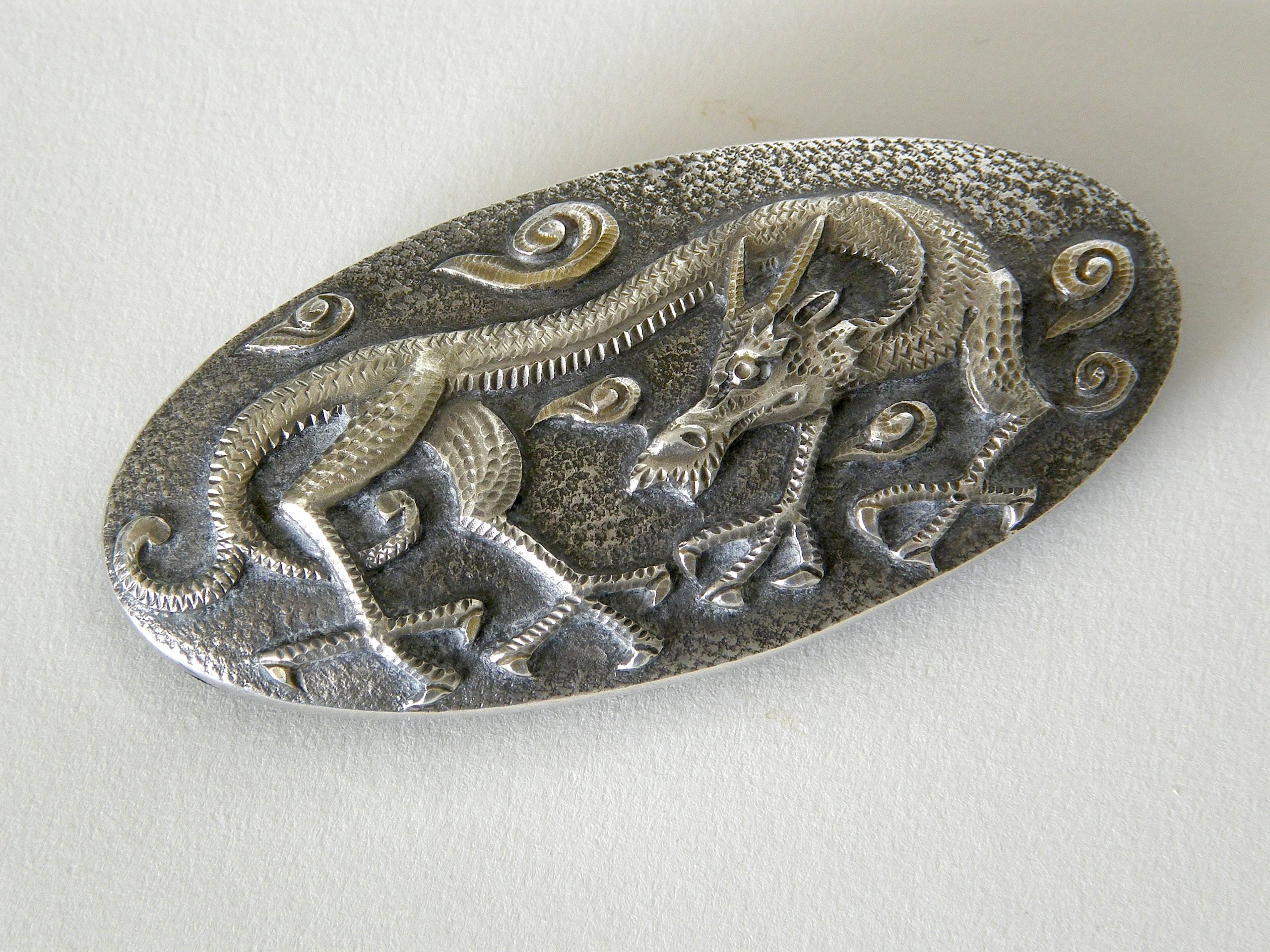 This wonderfully detailed, hand hammered belt buckle features a stylized dragon with huge claws and a forked tail. Abstract clouds swirl in the background. The design is rendered in relief with a three-dimensional effect. 

The front of the buckle
