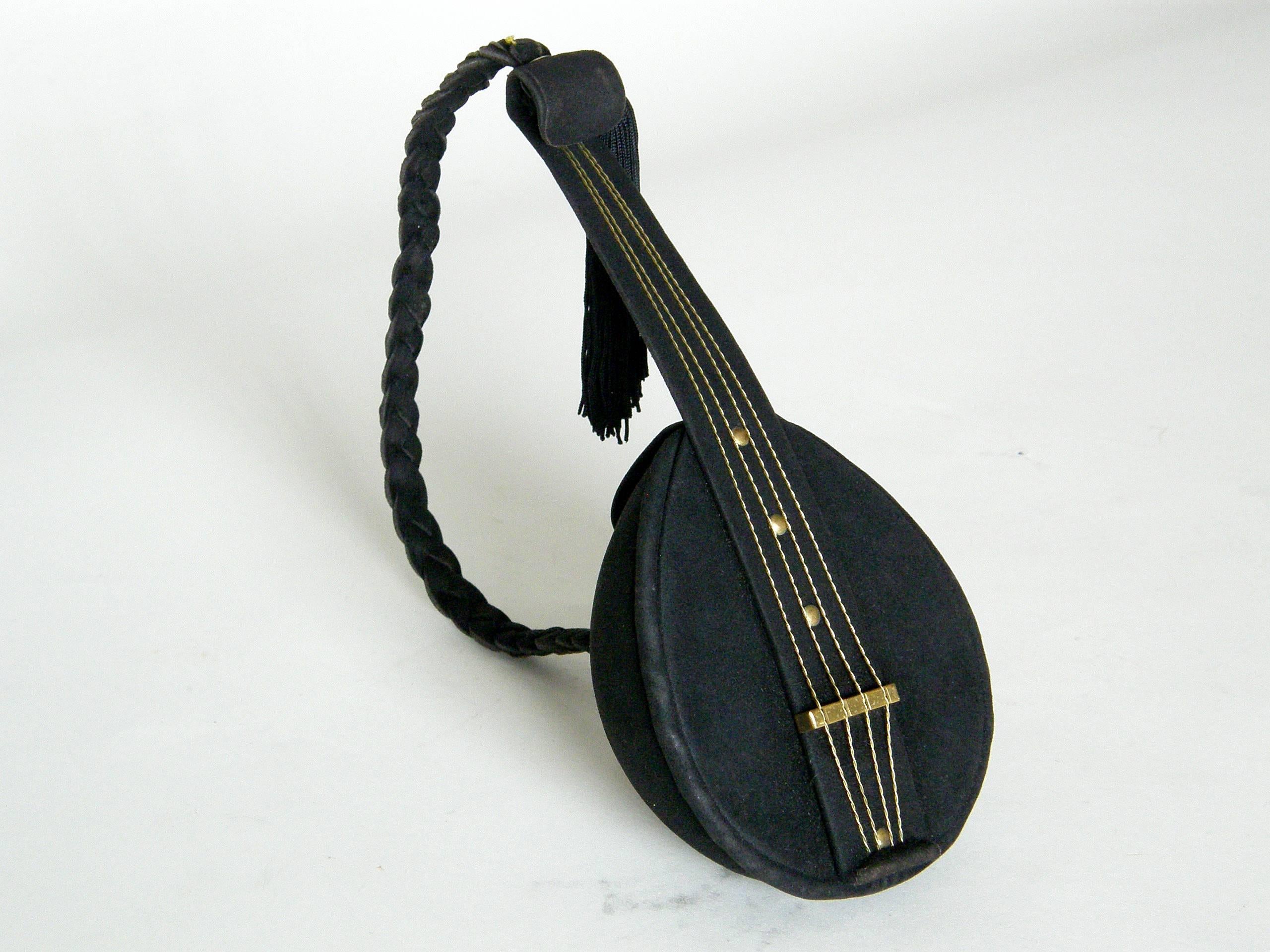 This delightful figural handbag is shaped like a mandolin. It's covered in a fine, black suede with details and accents in gold plated brass. The “strings” are twisted wires that run through notches in the “bridge”. The neck bends slightly and