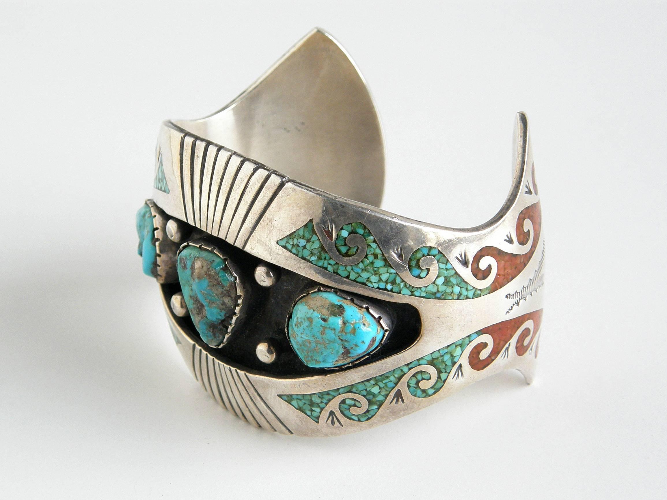 Sterling cuff bracelet by Navajo jewelry artist Charlie Singer set with three turquoise stones in a central shadowbox area and decorated with coral and turquoise chip inlay mosaic designs and tooled accents.

approximate measurements:
interior