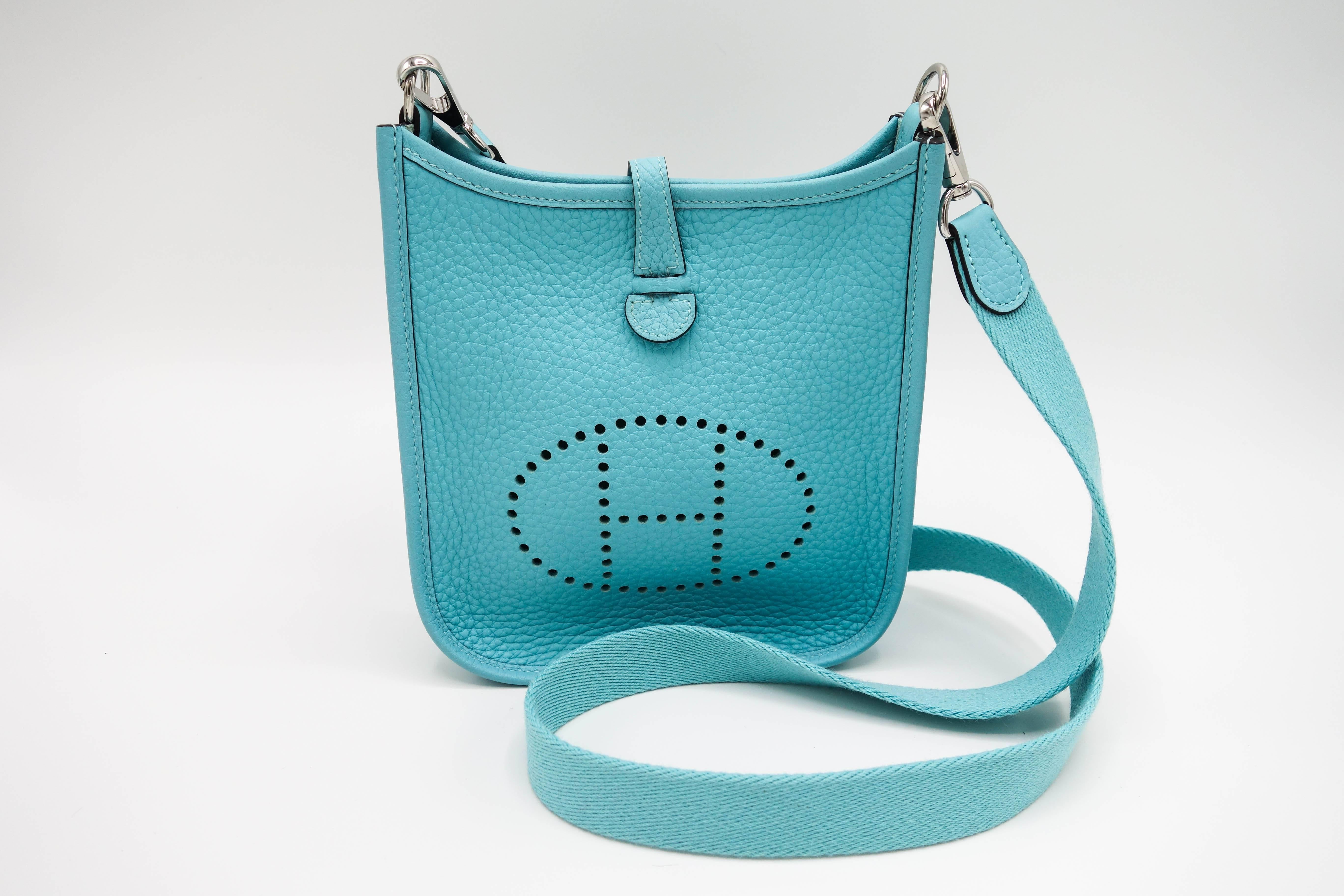 New in box rare Hermès Blue Atolle Mini Evelyne Clemence cross body bag with palladium hardware.  The mini Evelyne has a large perforated iconic "H" in a circle at the front, a top closure that has a snap at the rear and matching