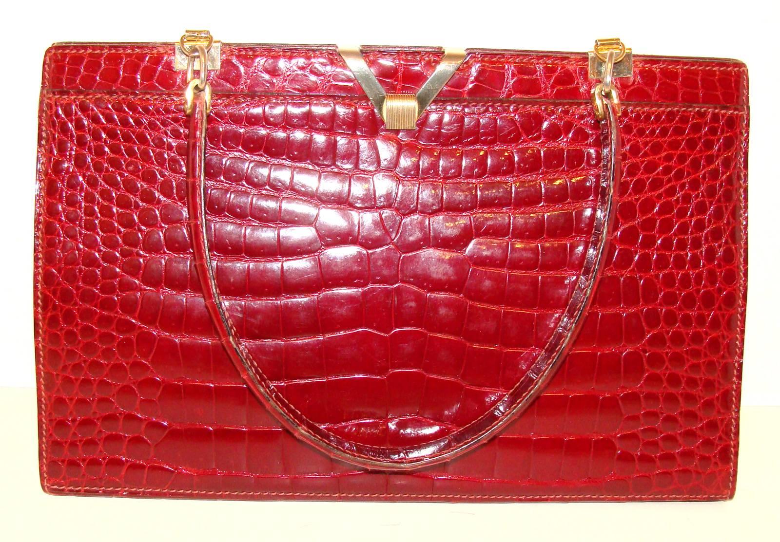This roomy alligator bag is from the 1950's.  The color is a deep red, similar to wine, but not as deep as a burgundy.  The front and back are both center skins and have rigid matching stitching.    There is a stylized G logo in gold which indicates