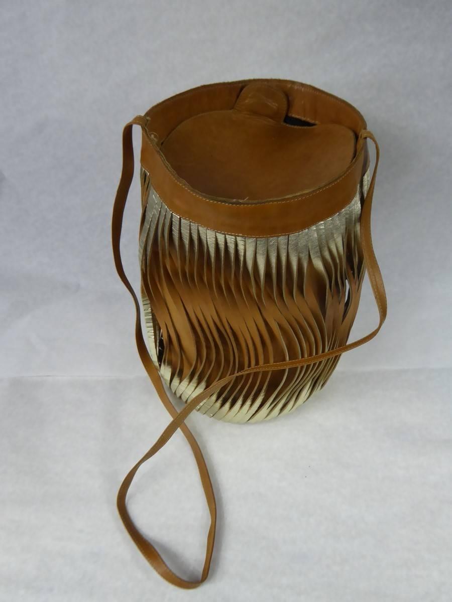 Circa 1970/1980

France

Maud Frizon

Lantern-shape bag, decorated with leather strips cut to make an effect of silver or gold twists as light changes.

Closes with a pressure valve in tan leather, large shoulder strap ( 110cm ) matching with cream