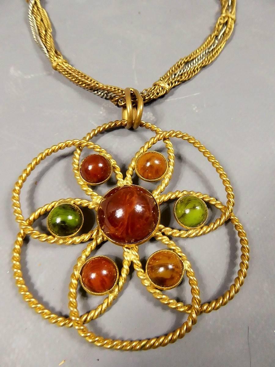 Circa 1970
France

Original Yves Saint Laurent Couture Pendant Necklace by Roger Scemama fromthe Seveenties. Rosace of two gold threads forming a flower. On each petal, stones of khaki green, amber and terracotta based on a golden background. In the