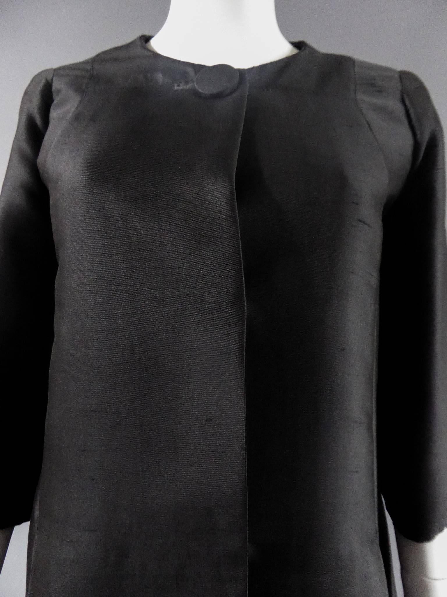Circa 1950

France

Haute couture coat late 50s by Jean Dessès in shiny black shantung silk. Cut in the continuity of the 1960s trapezoidal line. Two folded bellows under the two side pockets. Button fastening similar to the collar and two snaps.