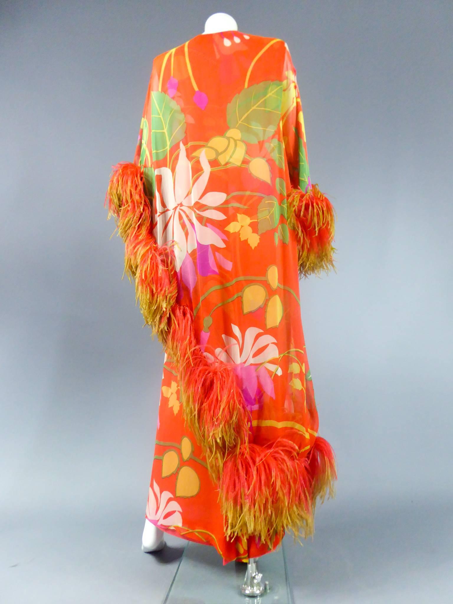 Circa 1975

France

Long tube and cape dress by Pierre Balmain Haute Couture in printed orange chiffon and tropical floral patterns. Sleeve and asymmetric cape similar underlined coral ostrich feathers in lime-green gradient. A nod to the colors and
