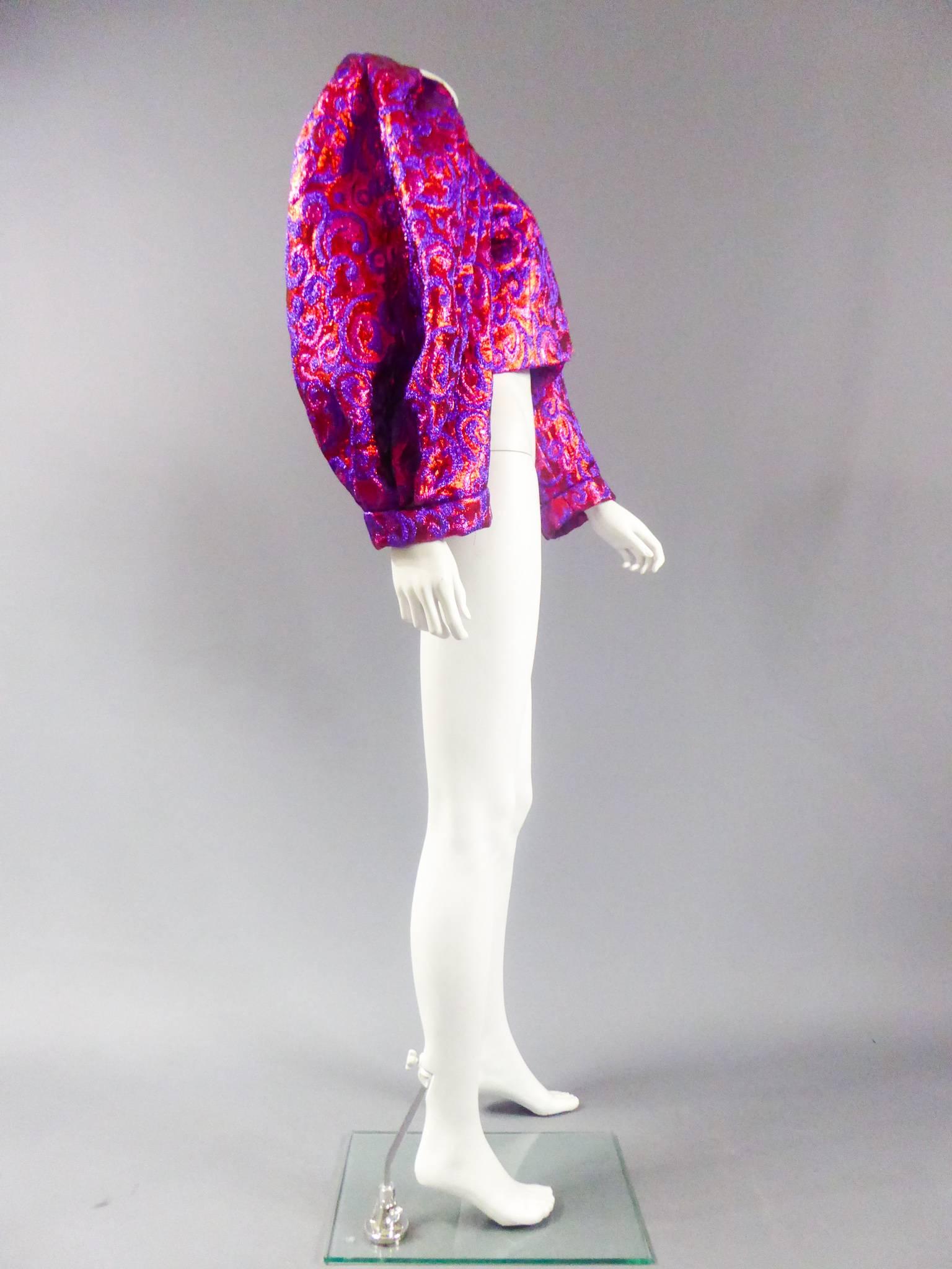 Winter 1989

Frankreich

Bolero aus Lurex in Fuchsia und Violett mit orangefarbenen und roten Akzenten:: Yves Saint Laurent Haute Couture Winter 1989. Florale Muster in Arabesken. Übergroße Ärmel:: anliegende Ärmel mit Hohlfalten an den Schultern::