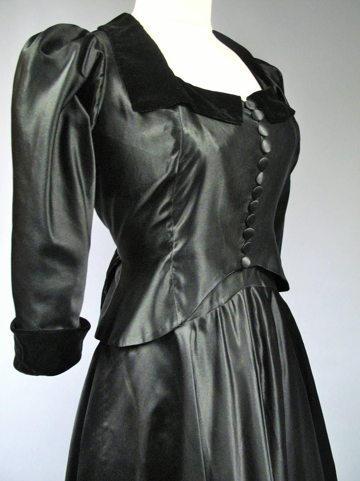 Um 1935
Frankreich Haute Couture
Abendkleid Haute Couture Maggy Rouff aus schwarzem Satin und Samt von 1935. Jacke mit Rundhalsausschnitt, Kragen und Aufschlägen aus schwarzem Samt, Puffärmeln und zwölf Knöpfen auf der Vorderseite. Das Mieder wird