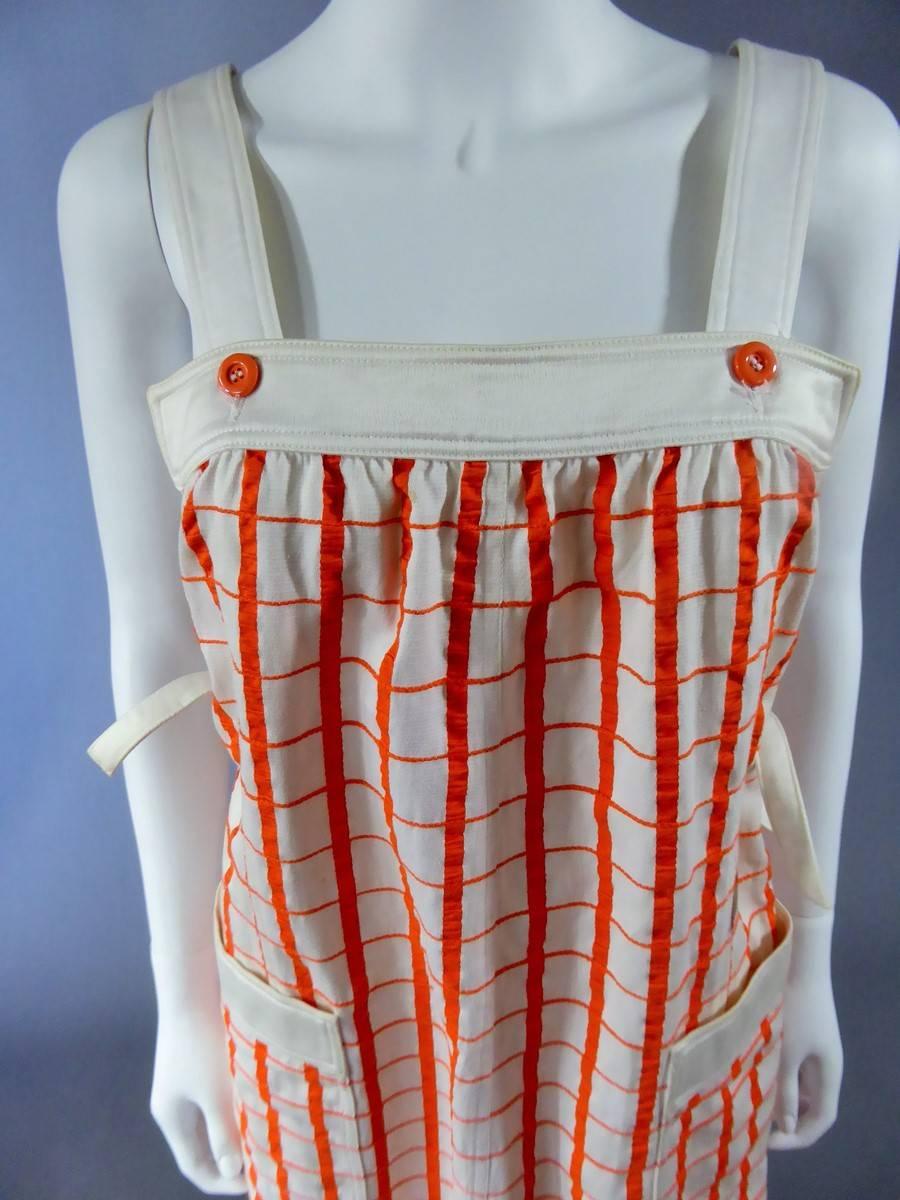 Circa 1965-1970

France
A line shape Haute Couture dress by André Courrèges. Model numbered 19055. Attached with two white straps hold by orange buttons on the face and on the back.
Pattern of the dress is checkered with orange lines on white