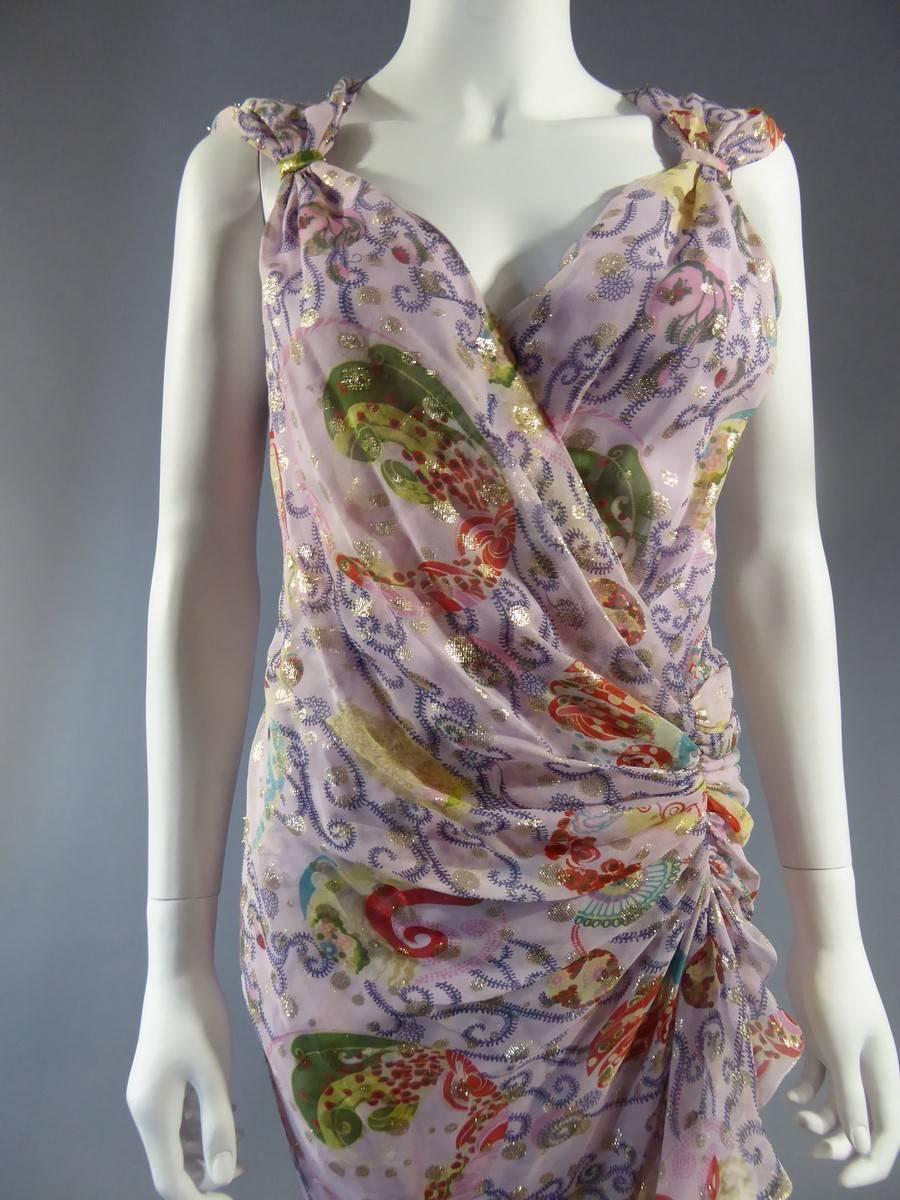 Circa 2000

France

Long dress in pale pink printed chiffon decorated with several floral patterns in green and red, embellished with "gold" threads. 
V-neck and straps with a small sail to the birth of the arm.
The dress presents a drapé