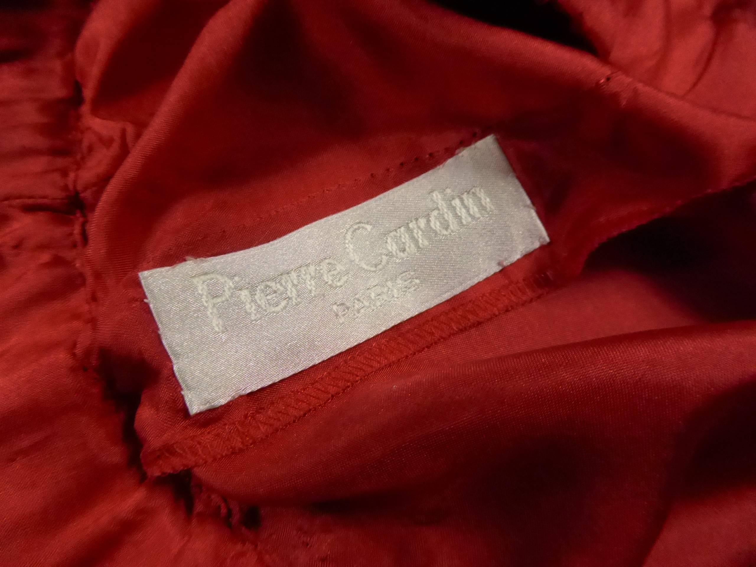 Early 1980.

France.

Pearly red dress from Pierre Cardin, in polyester satin, inner lining in red viscose. Under skirt held by two black presses inside the dress. Large three quarter batwing sleeves. Split on top of arms and closed by a small knot
