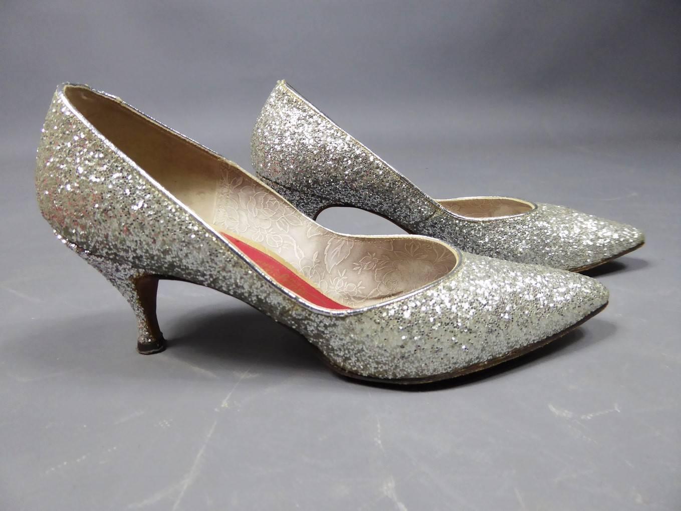 Pair of Schiaparelli silver glitter shoes in leather dating from the 1950s. Heel reel and pointed toe. Interior decorated with flowers and soles signed with a red label with Schiaparelli written in gold. Shoe box in shocking pink, emblematic