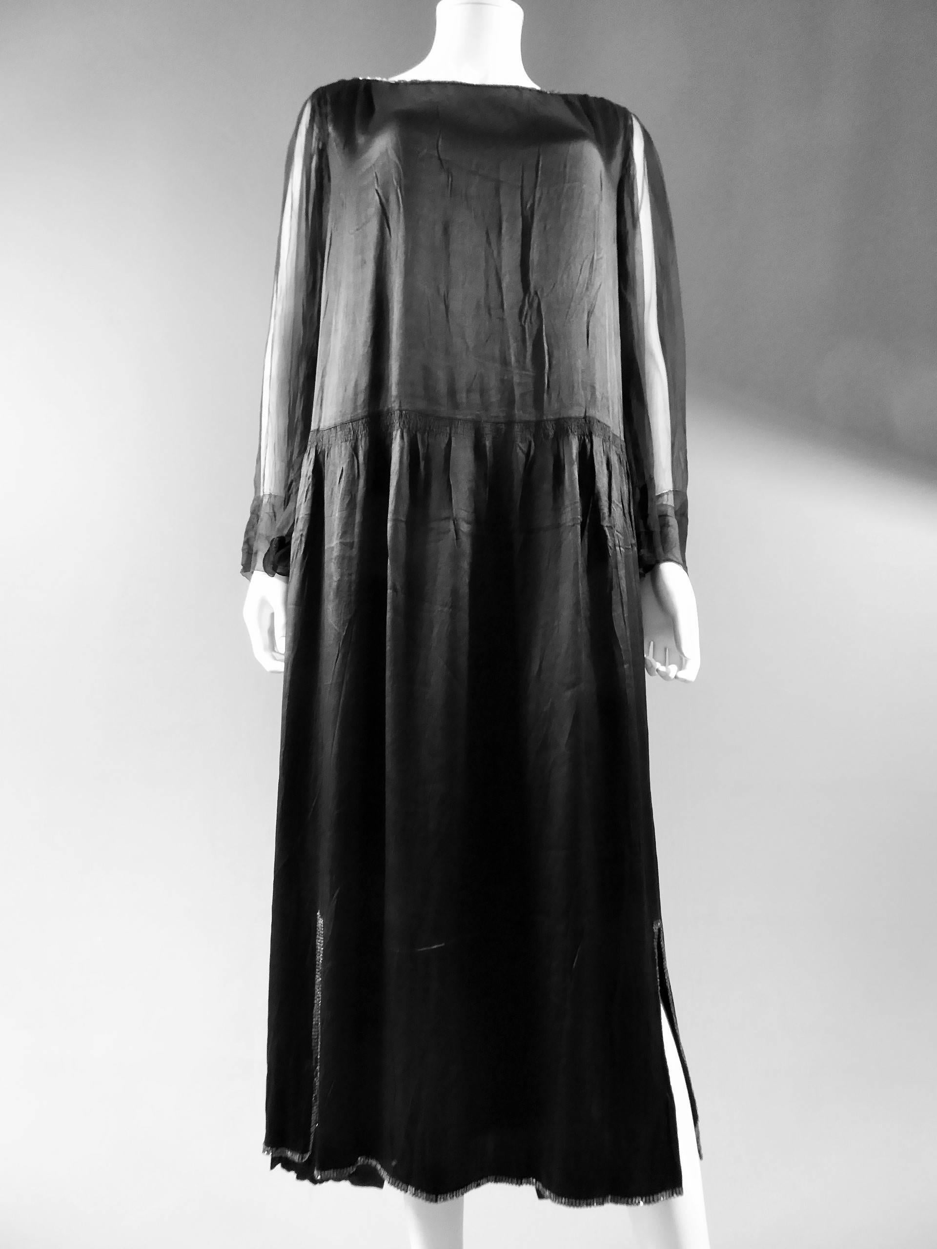 Circa 1920.

France.

Robe longue en crêpe de soie noir de Jeanne Lanvin Haute Couture. Forme large avec le dos de la robe plus long que le devant. Ajustement de la jupe, fendue sur les côtés en bas, avec 7 rangées de fronces montées à la pointe