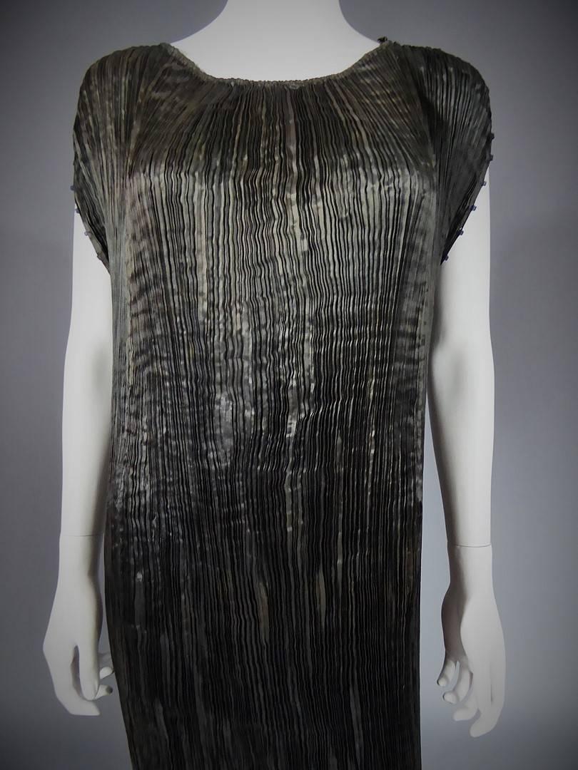 Circa 1920
Italy
Anthracite silk Delphos dress by Venetian couturier Mariano Fortuny. One piece dress finely pleated, made using a technique still unmatched today. Attached by dark blue ties on sleeves embellished by mate Murano glass tubular beads