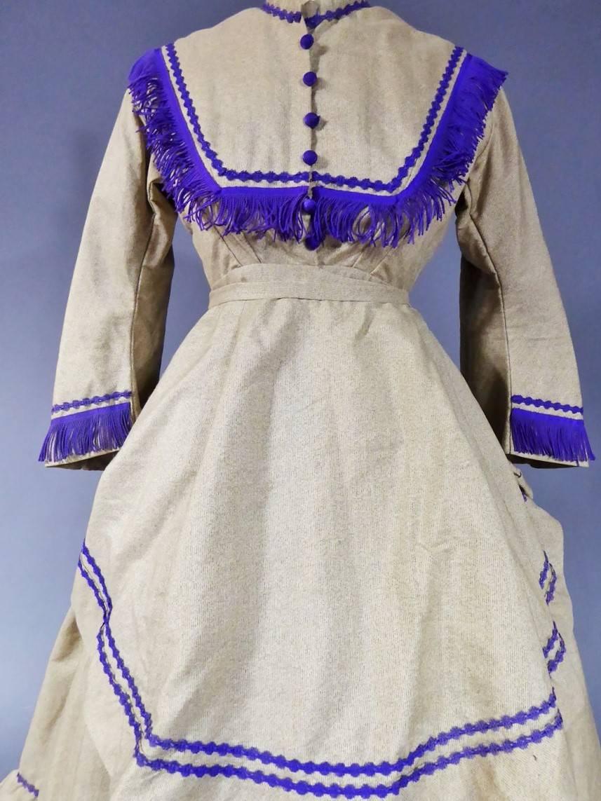  Circa 1855/1865

France

Beautiful crinoline woolen dress (for promenade or traveling) in wool cloth dating back from the Second French Empire. Beige and grey melange wool, with fringed trimmings and purple fringes. Pagoda sleeves, three rows of