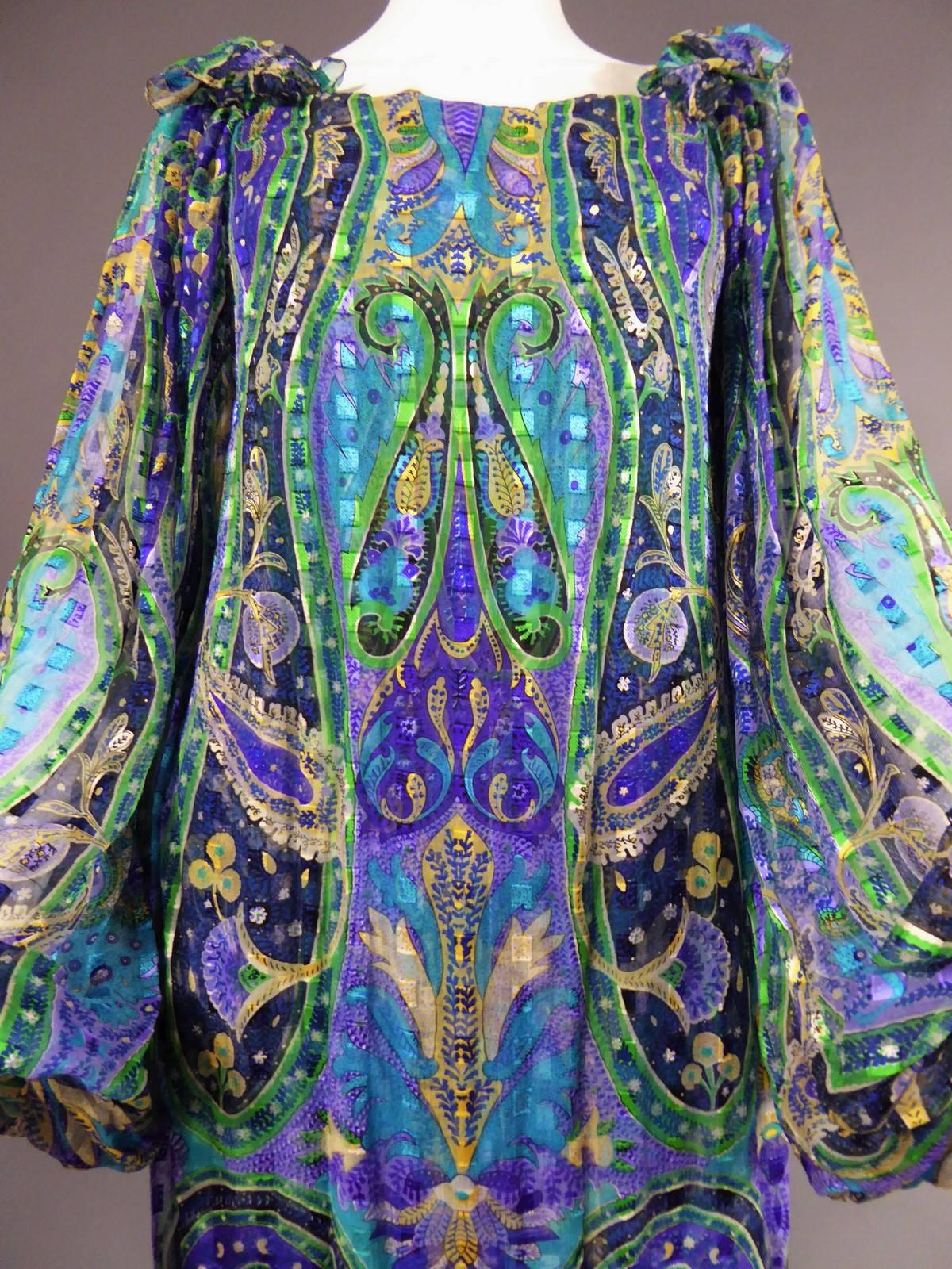 Circa 1970.

France

Carven long dress. Under dress in turquoise blue jersey with a split on the left side. Printed silk dress with Paisley pattern and botehs in the colors of a peacock: blue, purple, yellow, green, black. Rectangle collar. Wide and